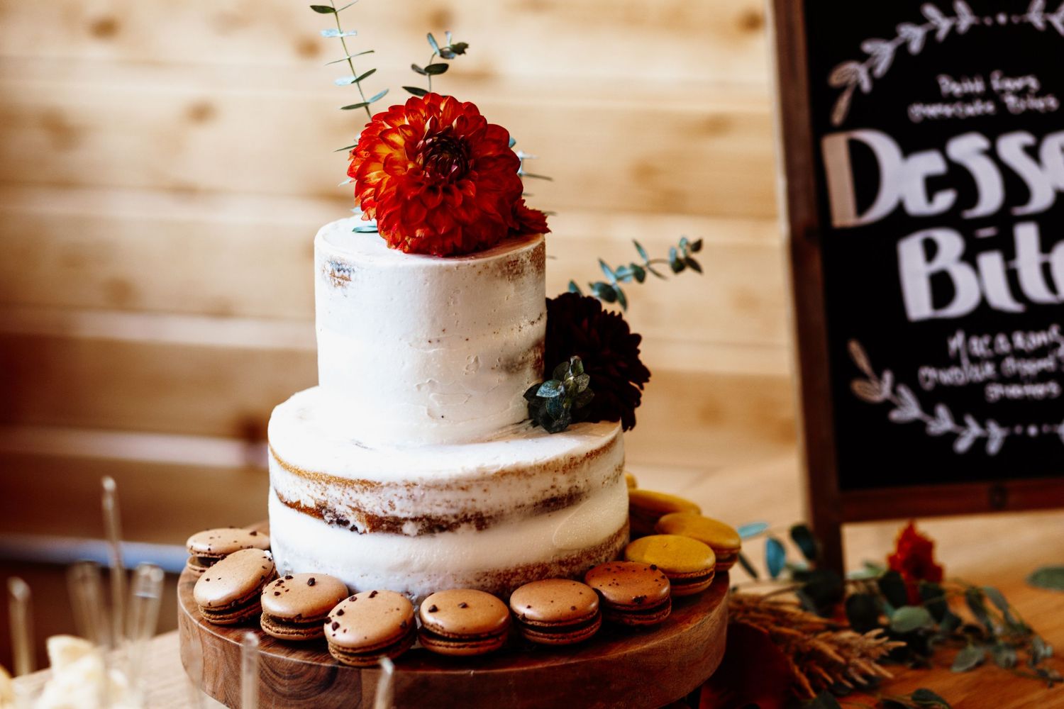 A rustic semi-naked wedding cake decorated with red and black flowers on a wooden cake stand.