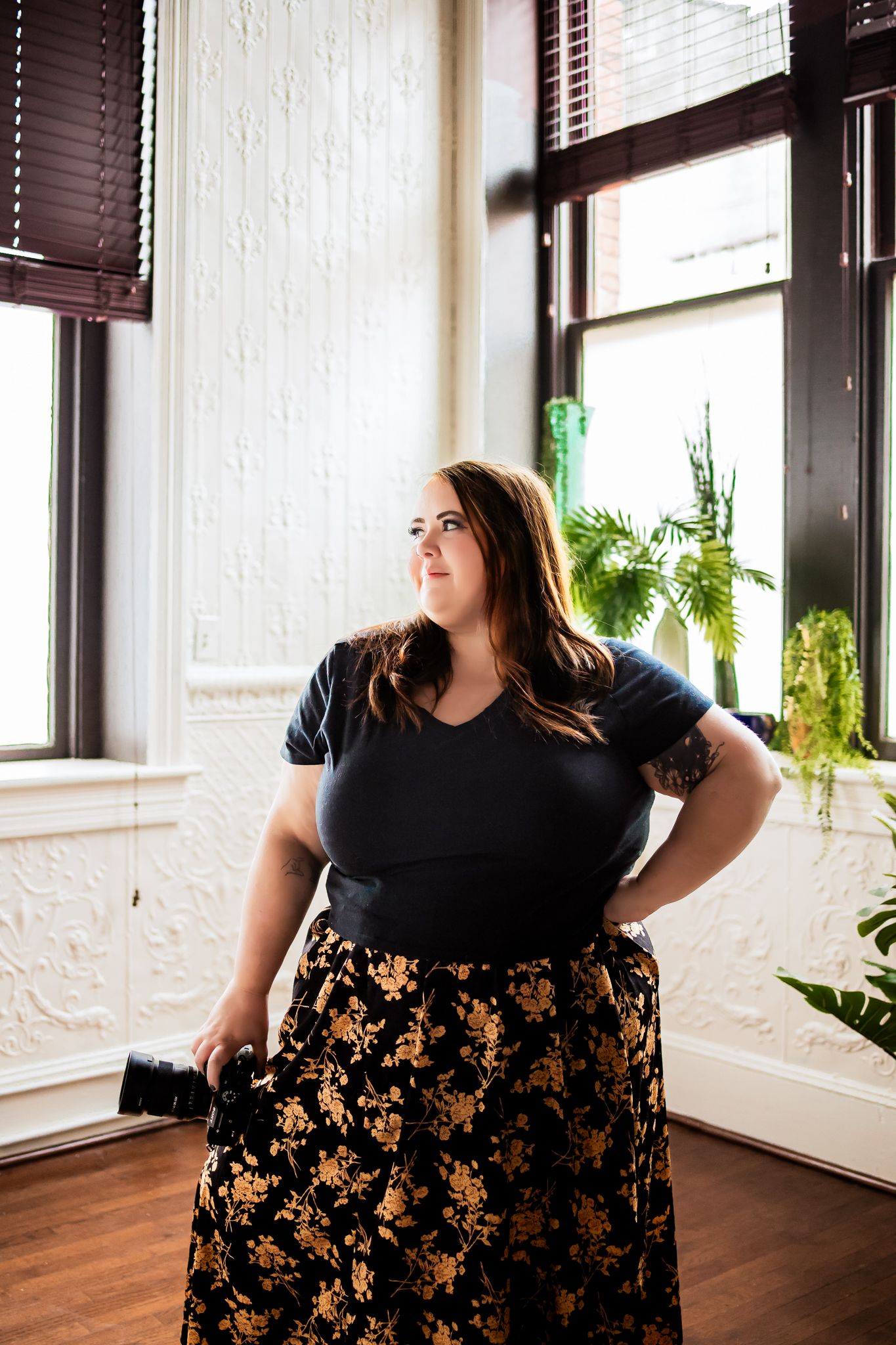 A lifestyle portrait in a bright corner room with wooden floors and white brick walls.
