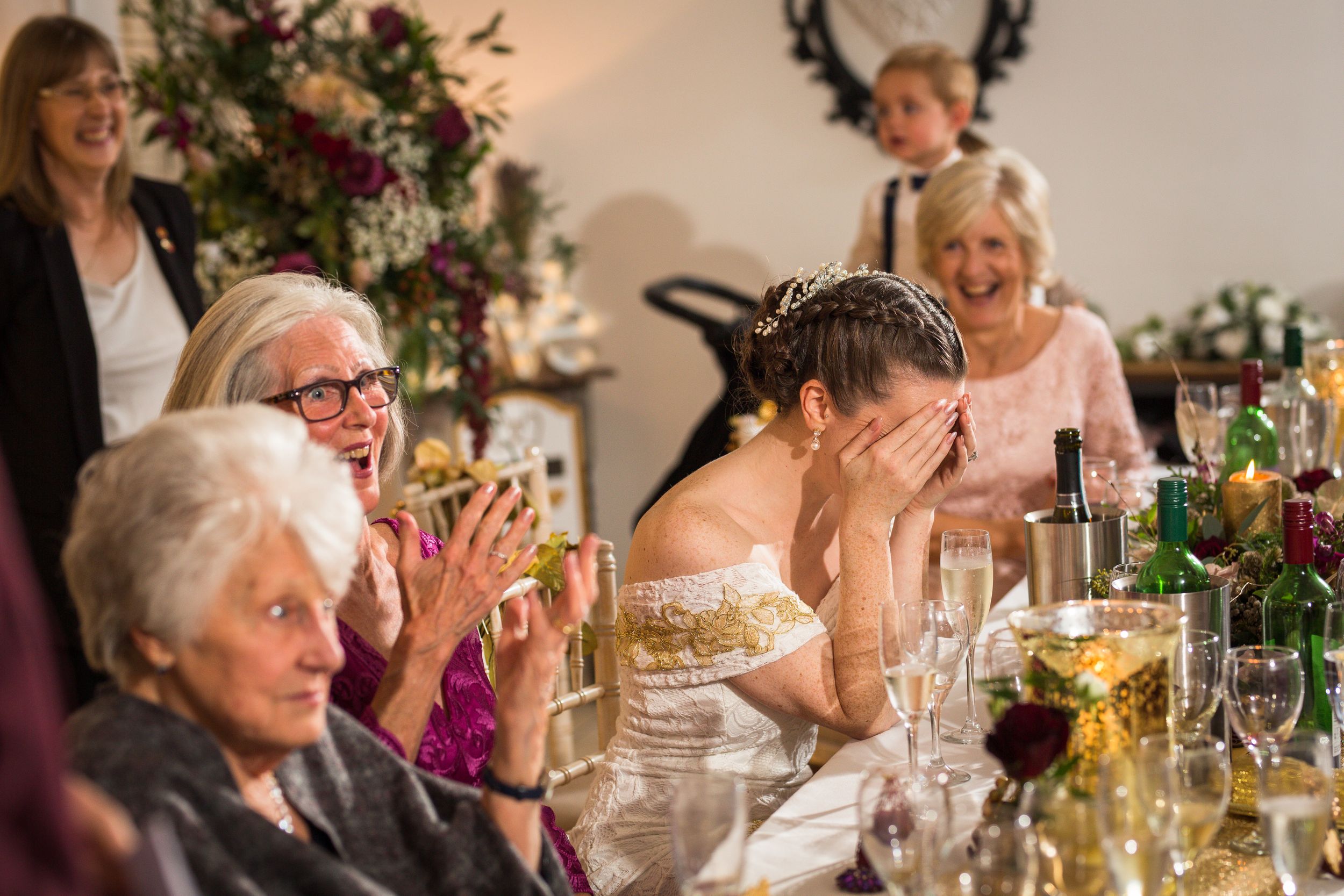 Emotional wedding reception moment captured with guests laughing and reacting at decorated dinner table.
