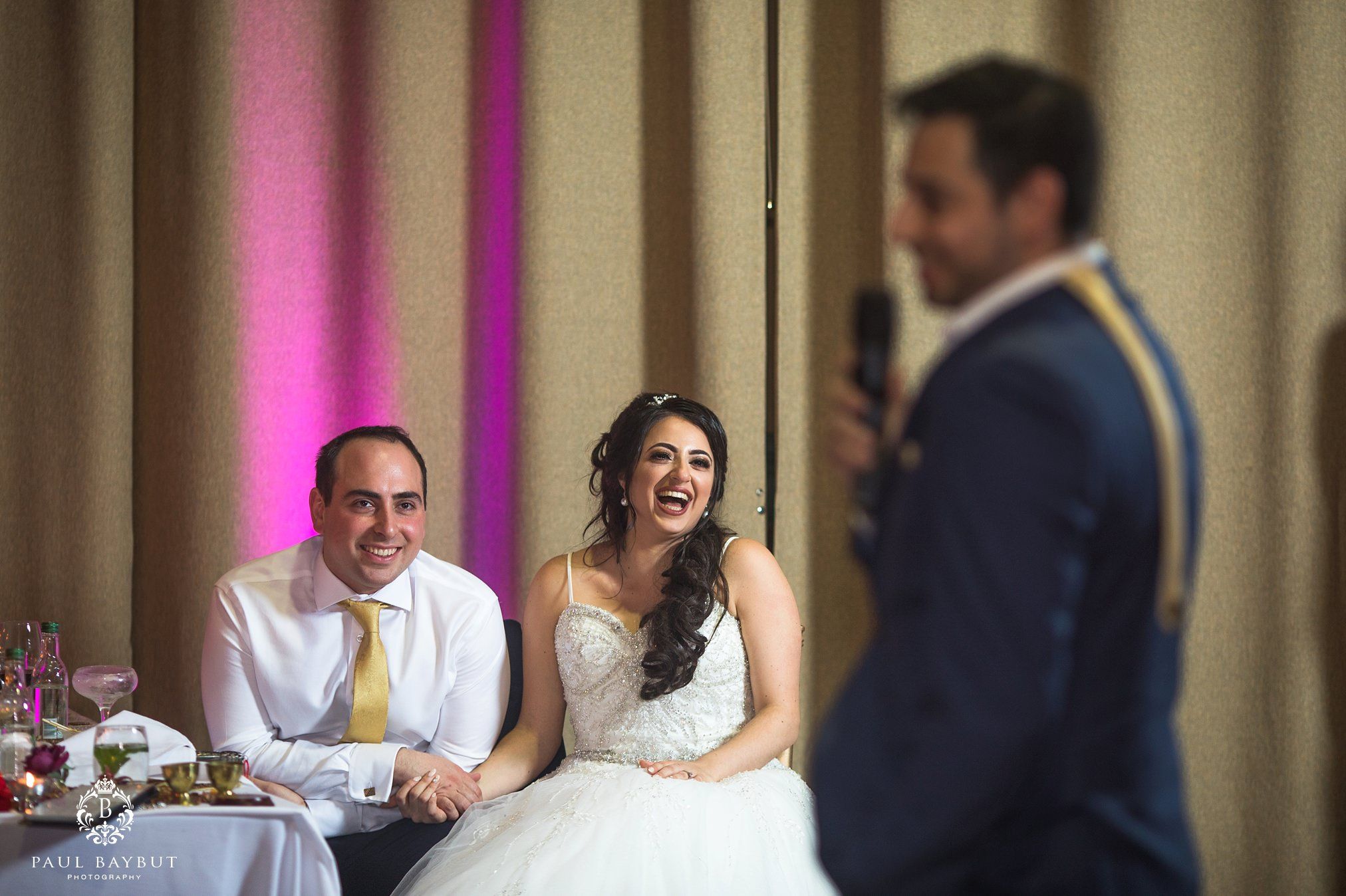 Wedding reception candid moment during speeches with guests seated at decorated tables.