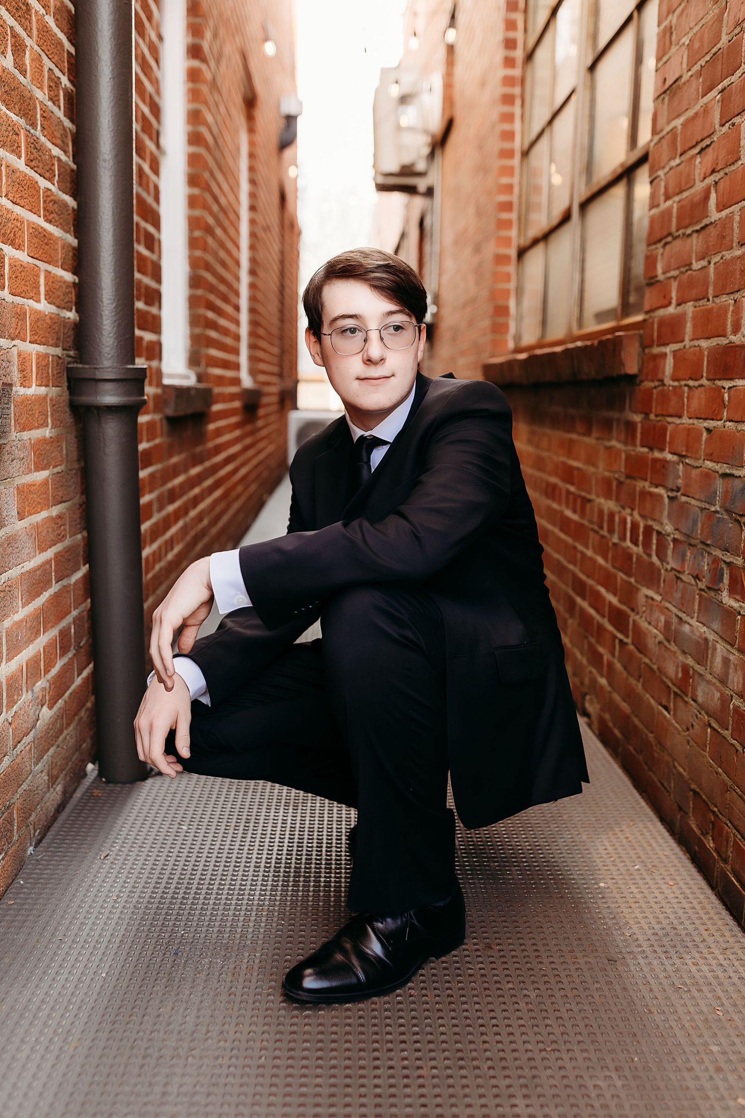 Professional portrait of a suited individual sitting in an urban brick alleyway.