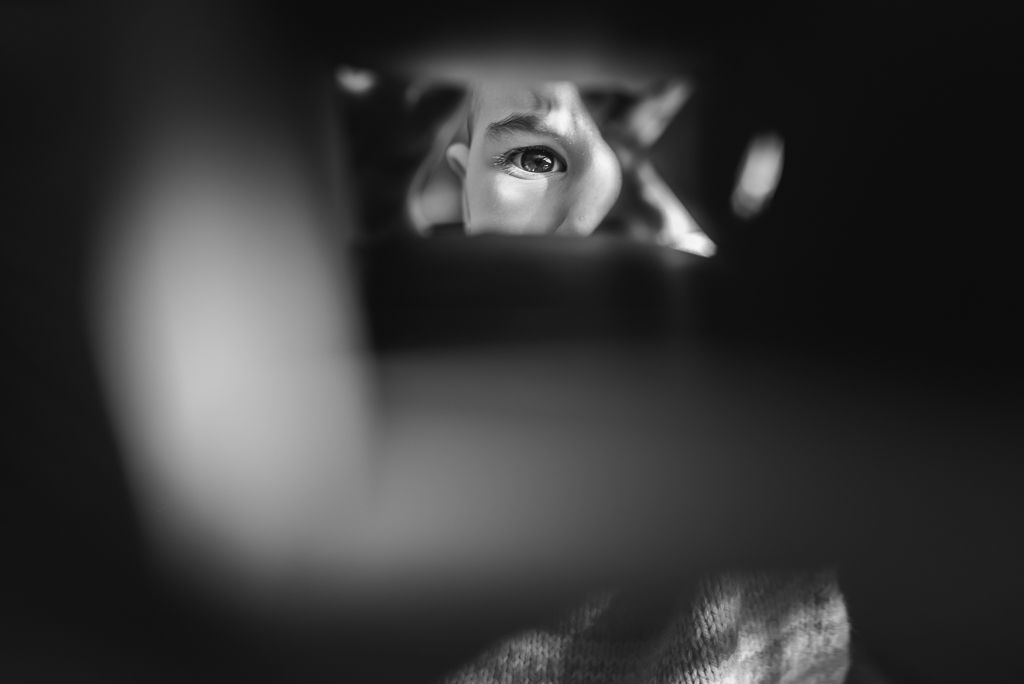 Black and white image of a young child as they look through a paper towel roll.