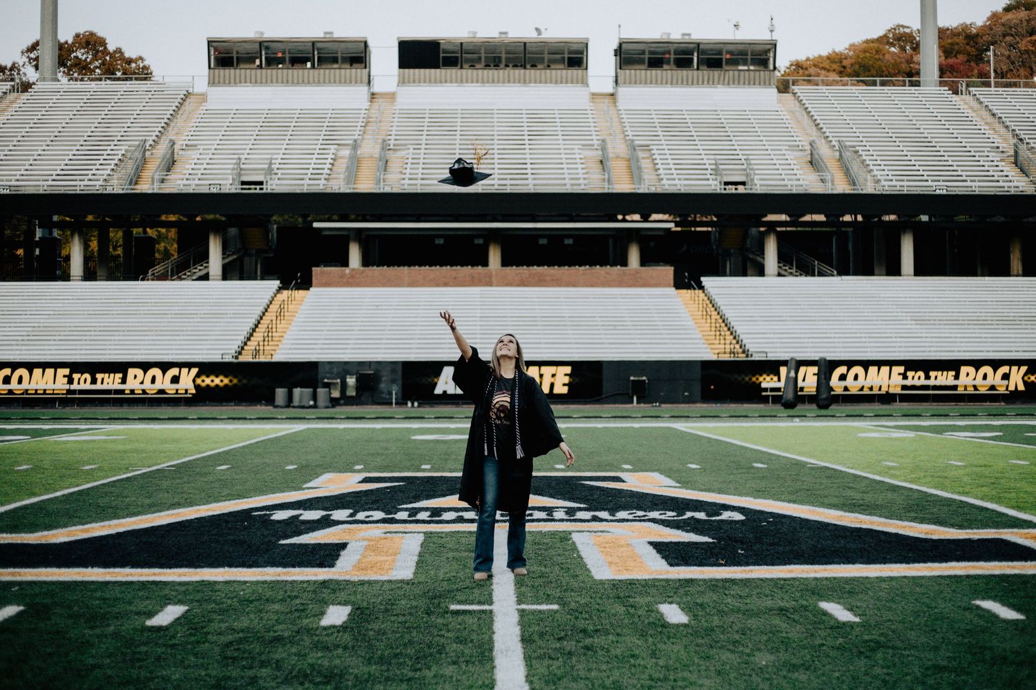 Person standing with arms raised on a football field in an empty stadium.