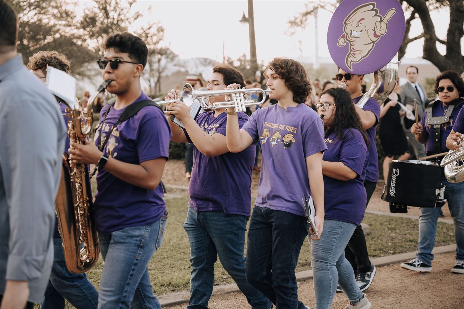 A marching band in purple uniforms performs while walking outdoors.