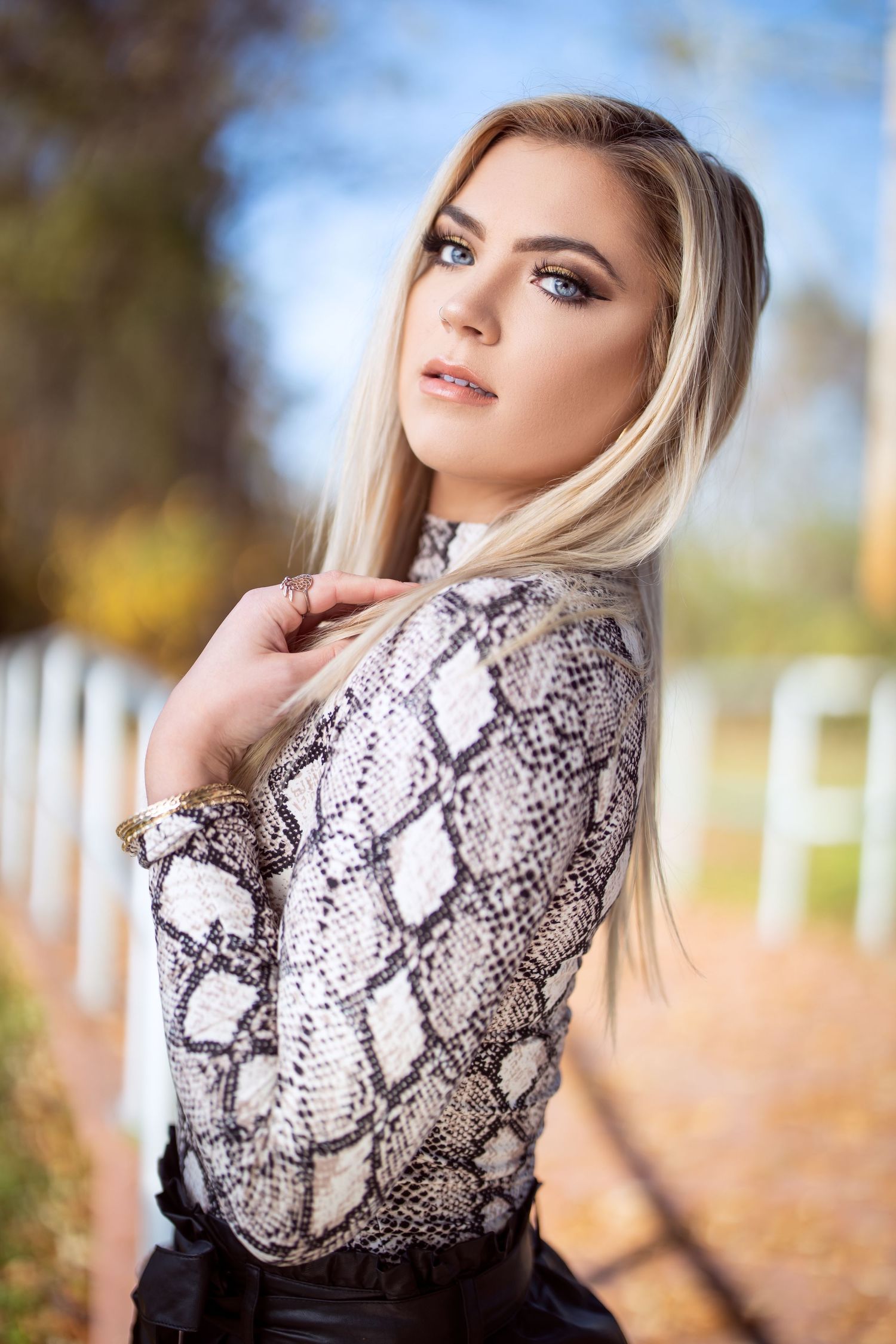 Close up portrait featuring snakeskin print top with autumn foliage backdrop.