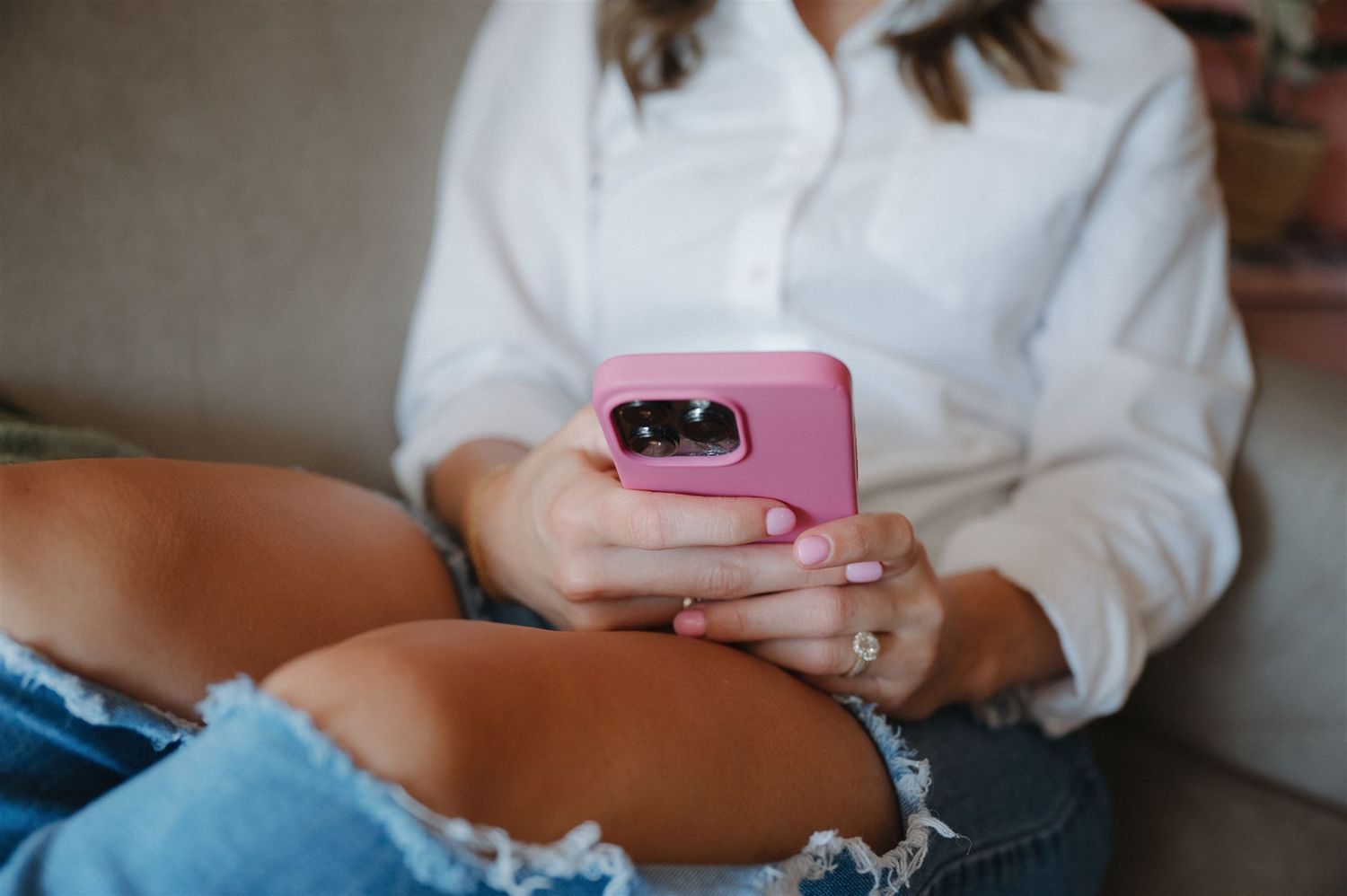Person in distressed jeans and white shirt sitting holding pink phone case.