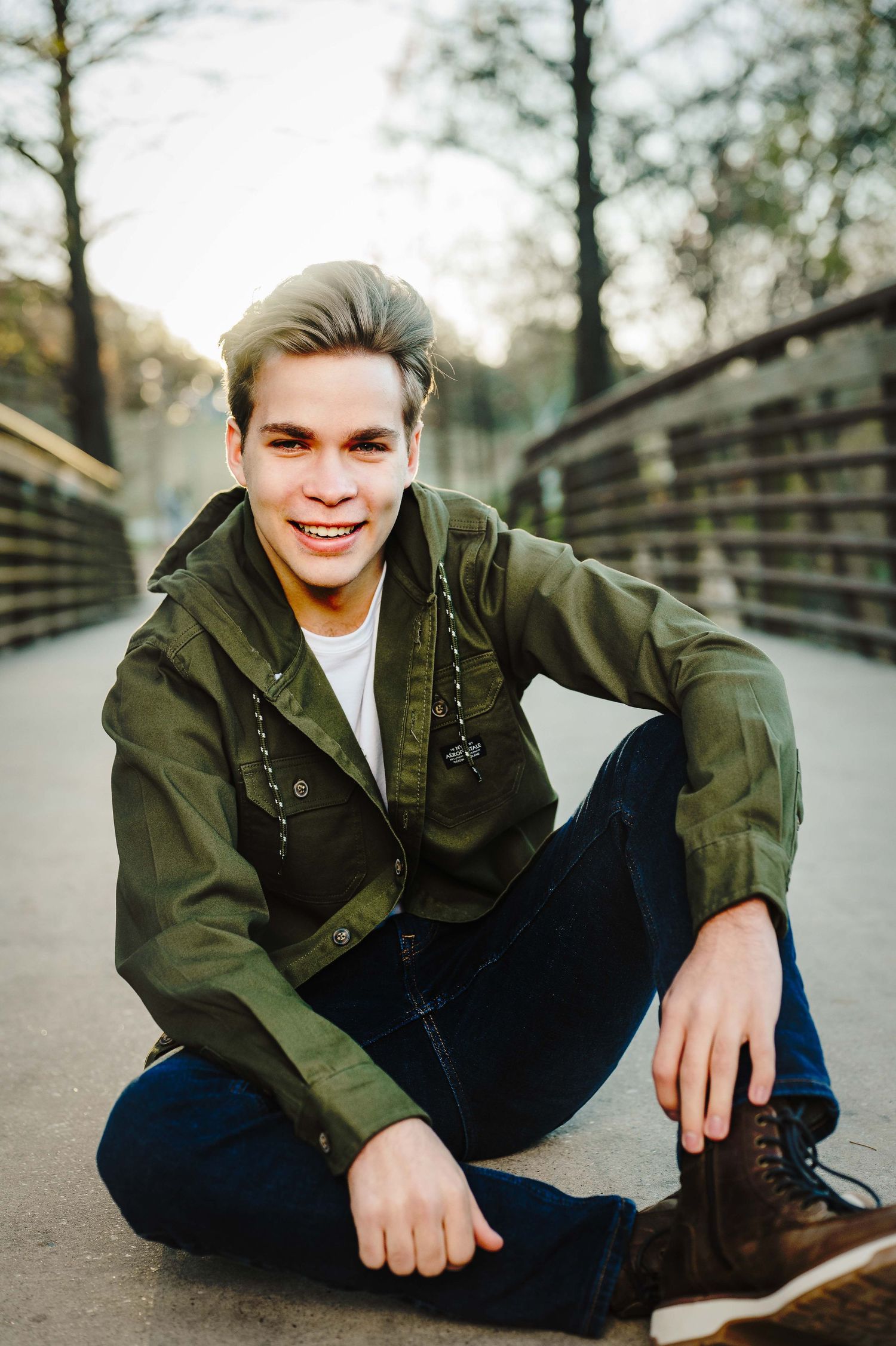 Casual outdoor portrait session featuring person in olive jacket and jeans on wooden walkway.