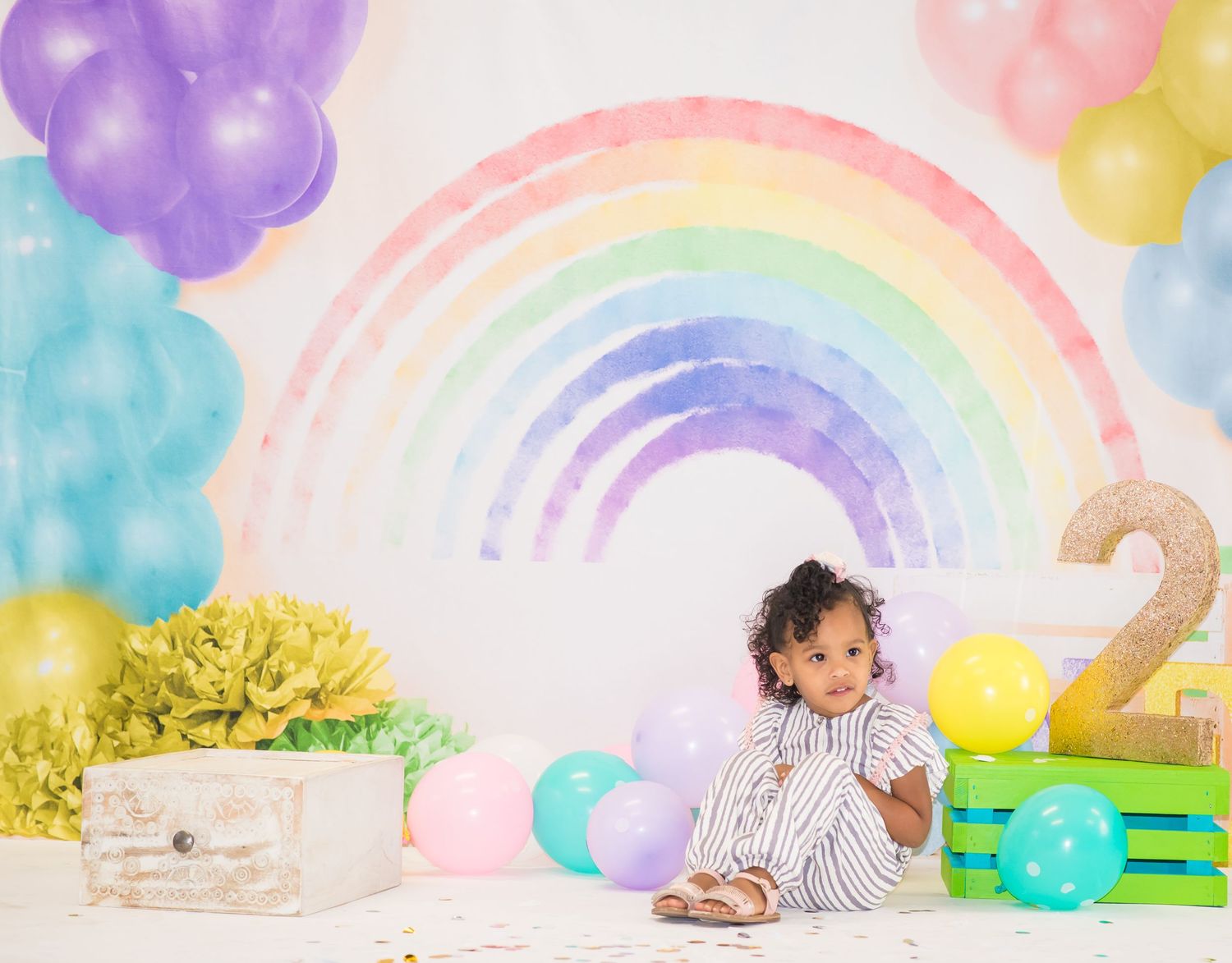 Rainbow themed second birthday photoshoot with pastel balloons and decorations.