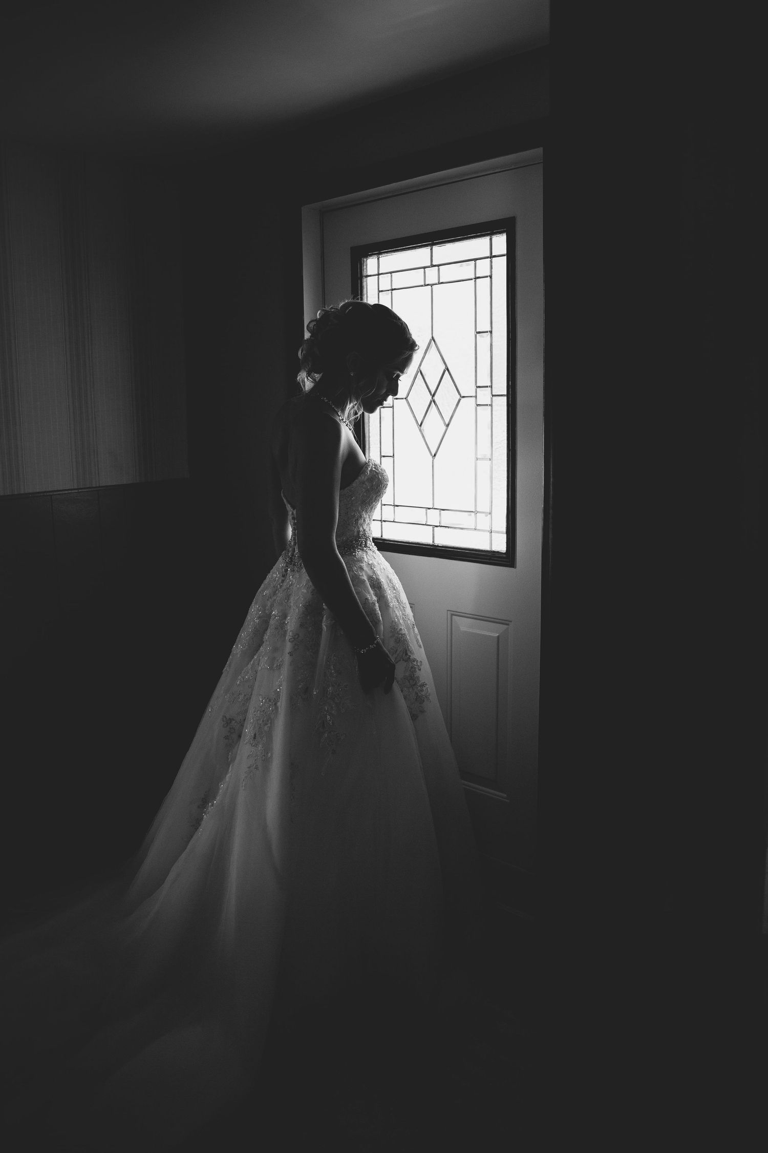 Artistic silhouette of bride in wedding gown standing by window with diamond pattern.
