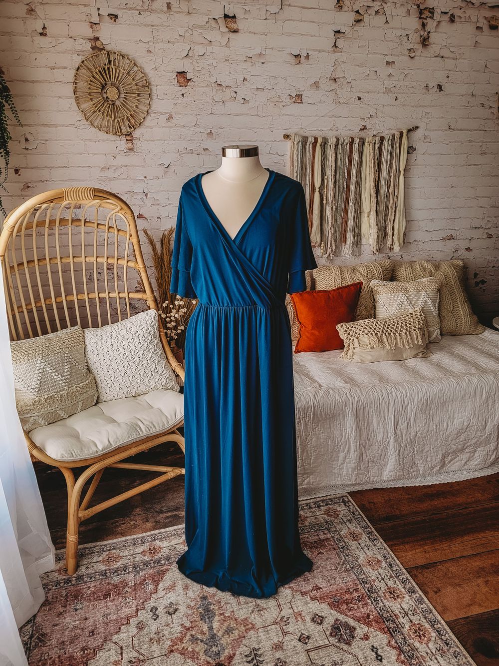 Teal blue wrap maxi dress with flutter sleeves displayed on mannequin in boho styled room.