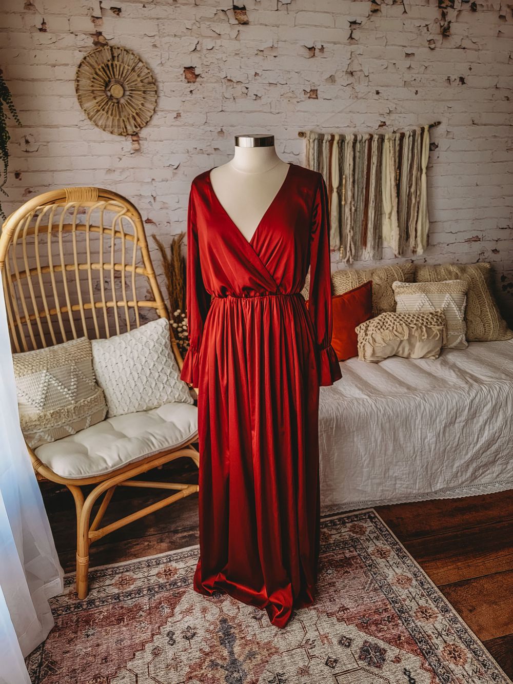 Elegant red satin wrap maxi dress with long sleeves displayed on mannequin in boho styled room.