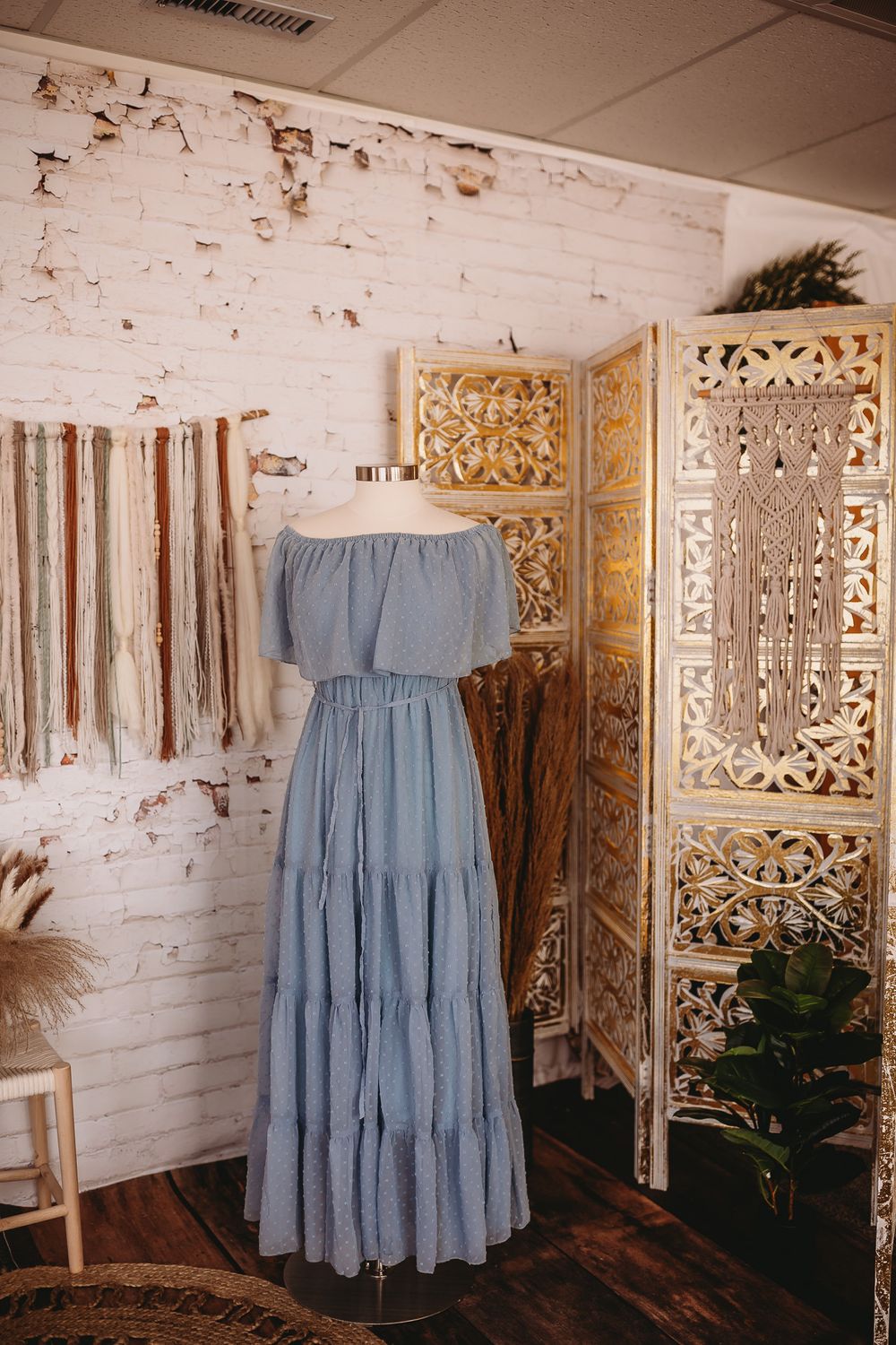 Light blue off-shoulder tiered maxi dress on mannequin in bohemian studio with white brick wall.