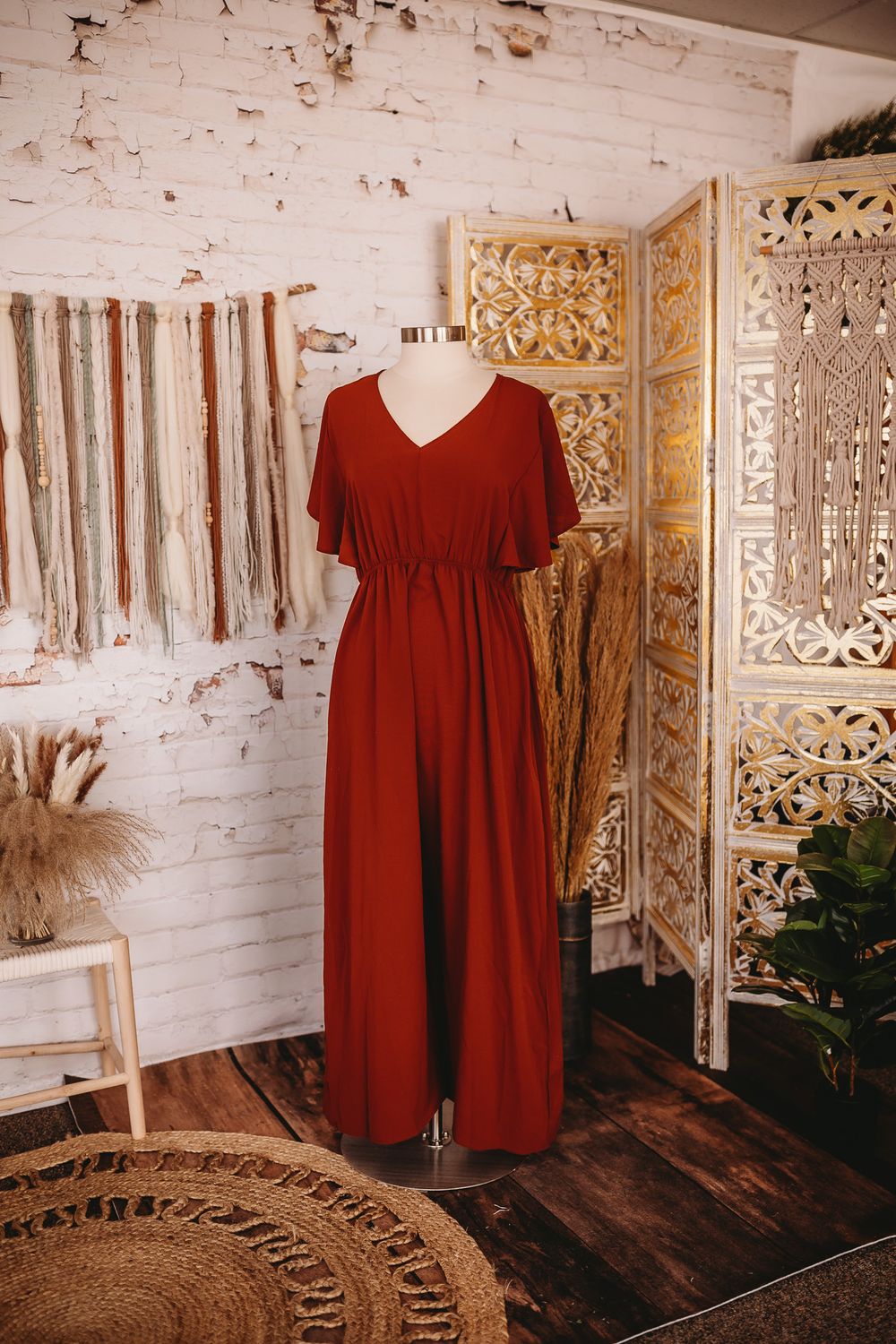Dark red flutter sleeve V-neck maxi dress on mannequin in bohemian studio with white brick wall.