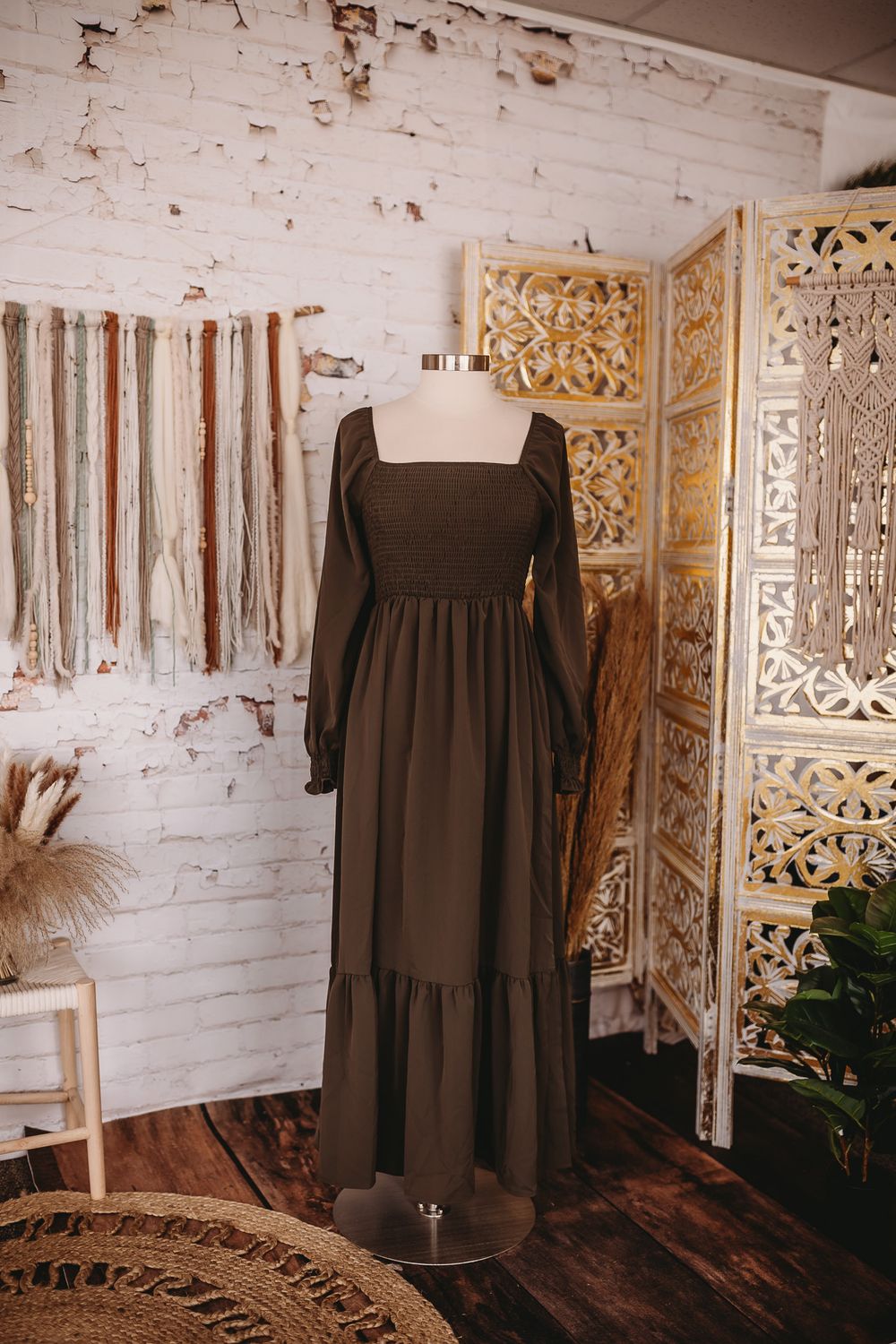 Dark olive green smocked bodice maxi dress with long sleeves on mannequin in boho studio.