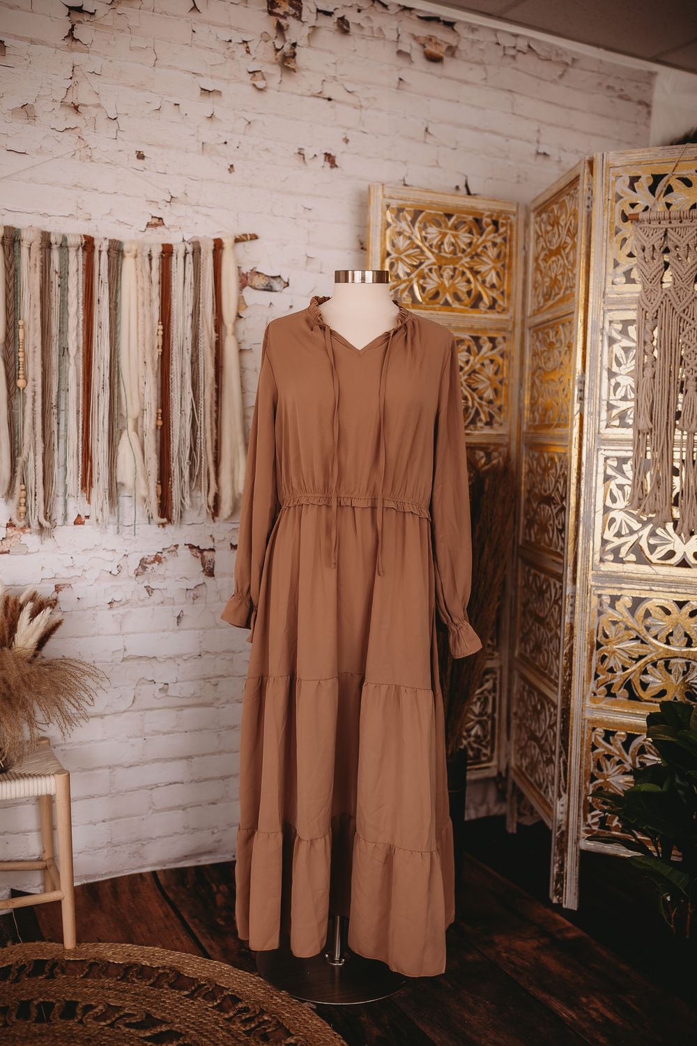 Camel brown tiered maxi dress with drawstring waist and long sleeves on mannequin in boho studio.