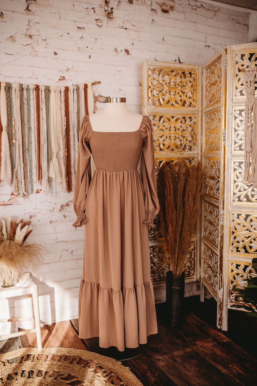 Light tan smocked bodice maxi dress with long puff sleeves on mannequin in sunlit boho studio.
