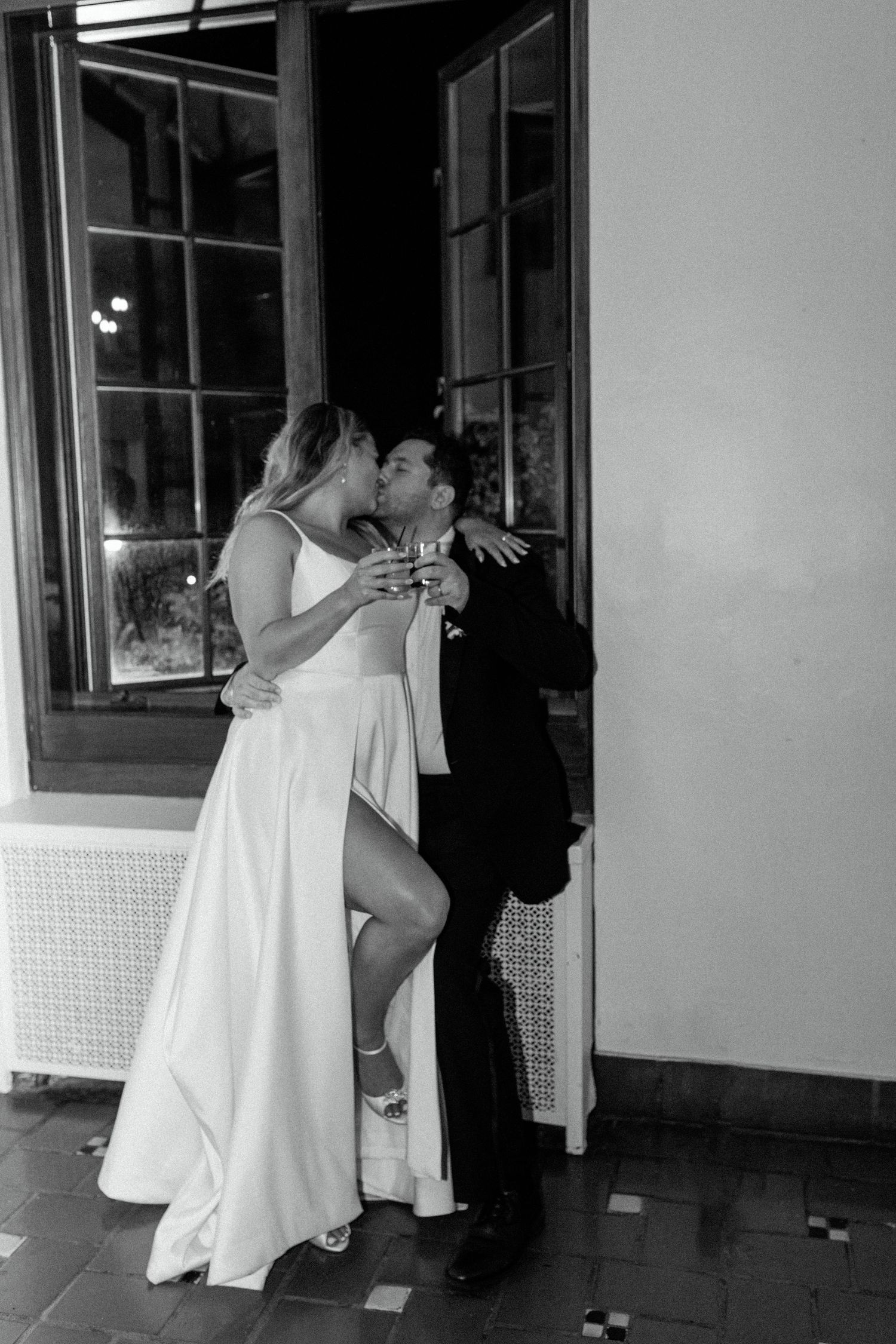 A black and white photo capturing an intimate moment between a couple by a window.