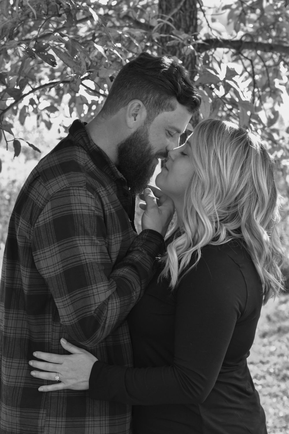 Romantic couple in plaid and black sharing intimate moments in wooded setting.