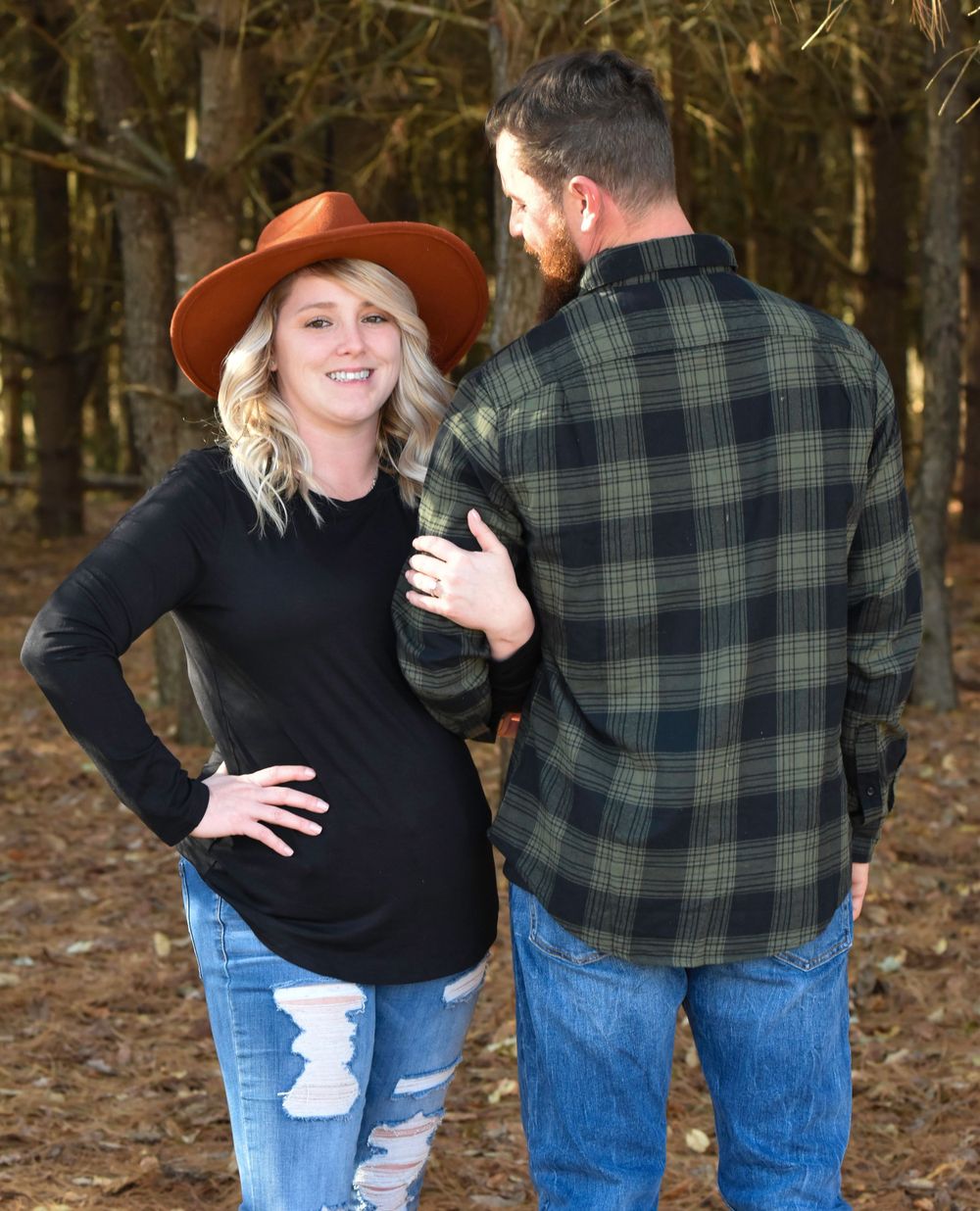Couple in autumn woods wearing jeans and casual wear posing playfully together.