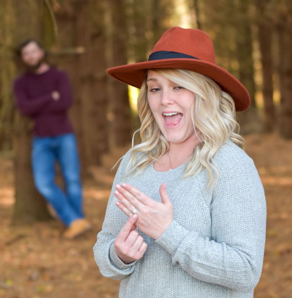 Woman in grey sweater and brown hat reacting joyfully to engagement proposal.