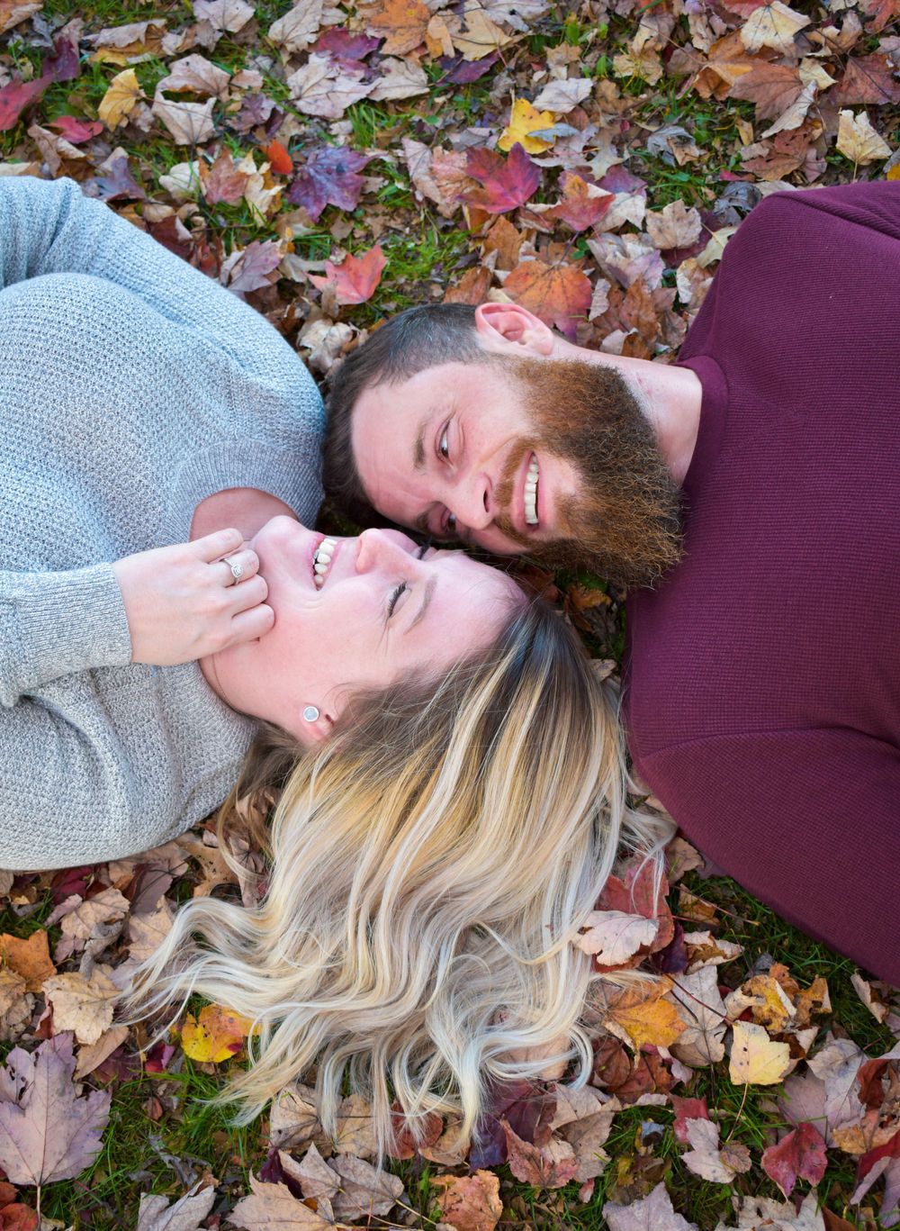 A couple lying in colorful autumn leaves smiling at each other.