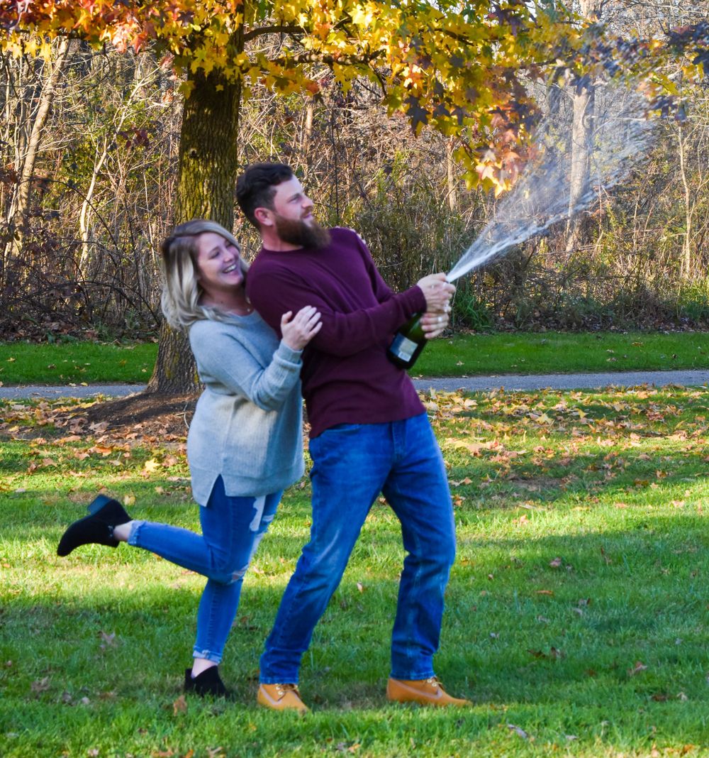 Playful couple in casual wear dancing and posing outdoors in autumn setting.