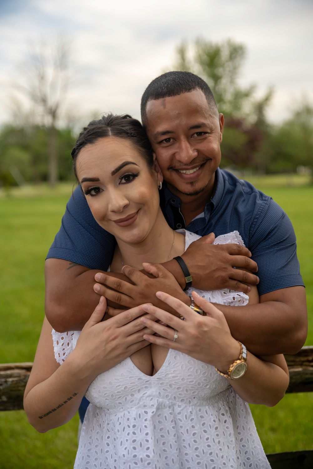 A couple shares an intimate embrace in a garden setting with natural greenery in the background.