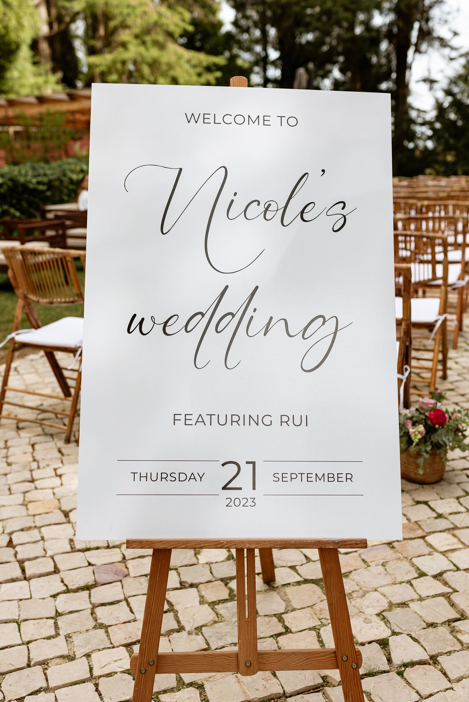 A white wedding welcome sign on a wooden easel displays elegant script text for a September 21st, 2023 ceremony, a wed at Quinta da Bichinha