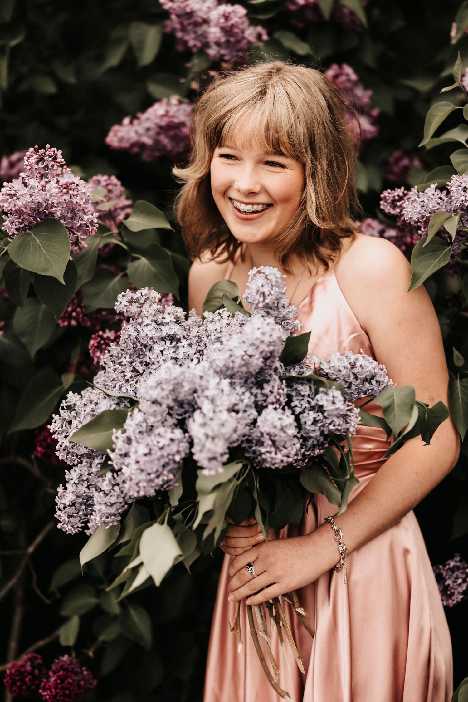 Natural candid laughter while holding fresh-cut lilac blooms in garden setting.