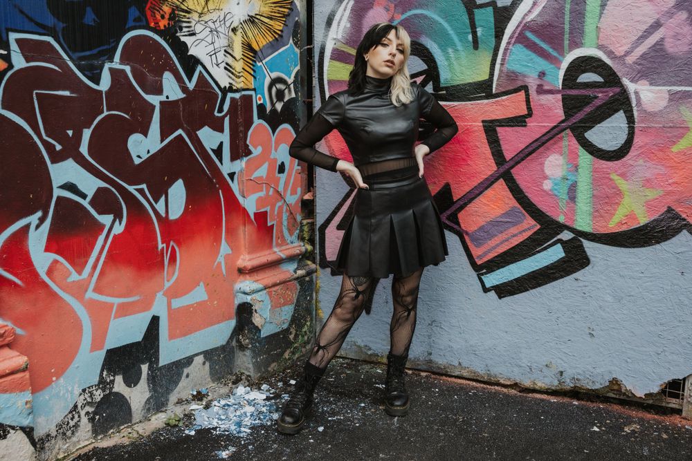Claudia leaning against a graffitied wall in Hove wearing a gothic outfit by Innocent Clothing