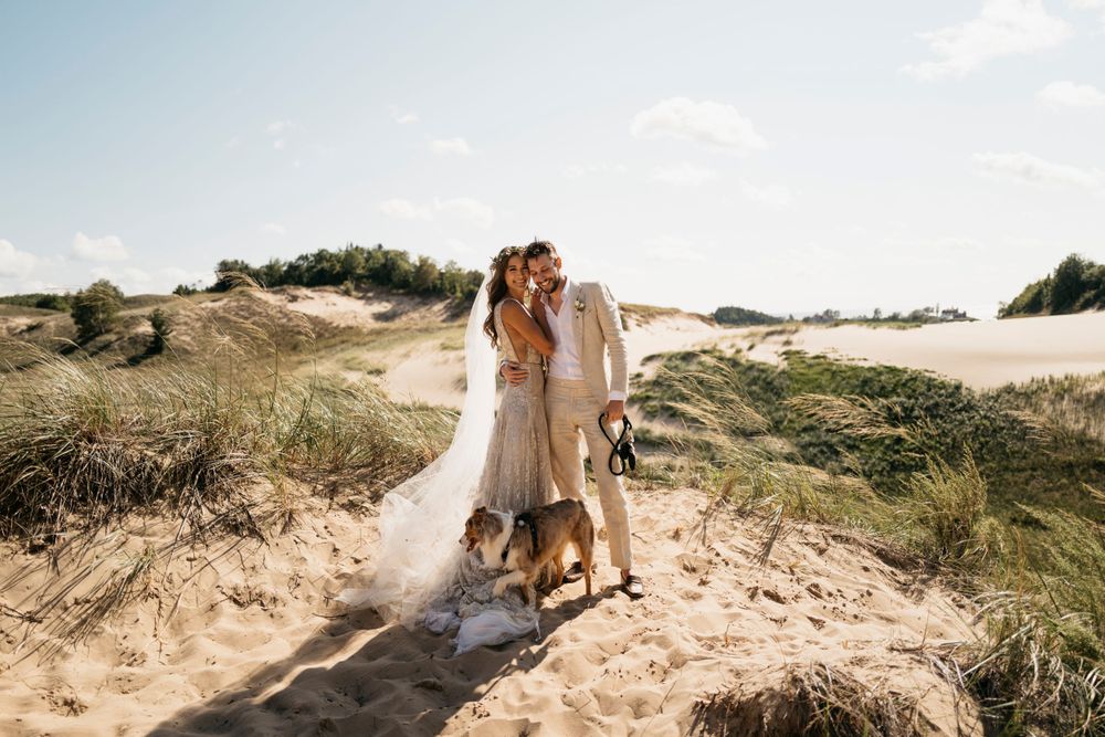 Bride and groom kissing with two dogs on sunny coastal sand dunes wedding photo.