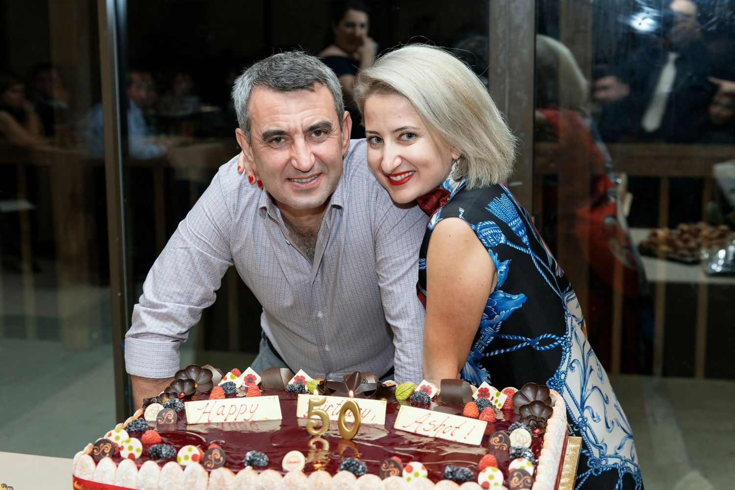 A couple smiling together behind a festive dessert display with decorated cakes.