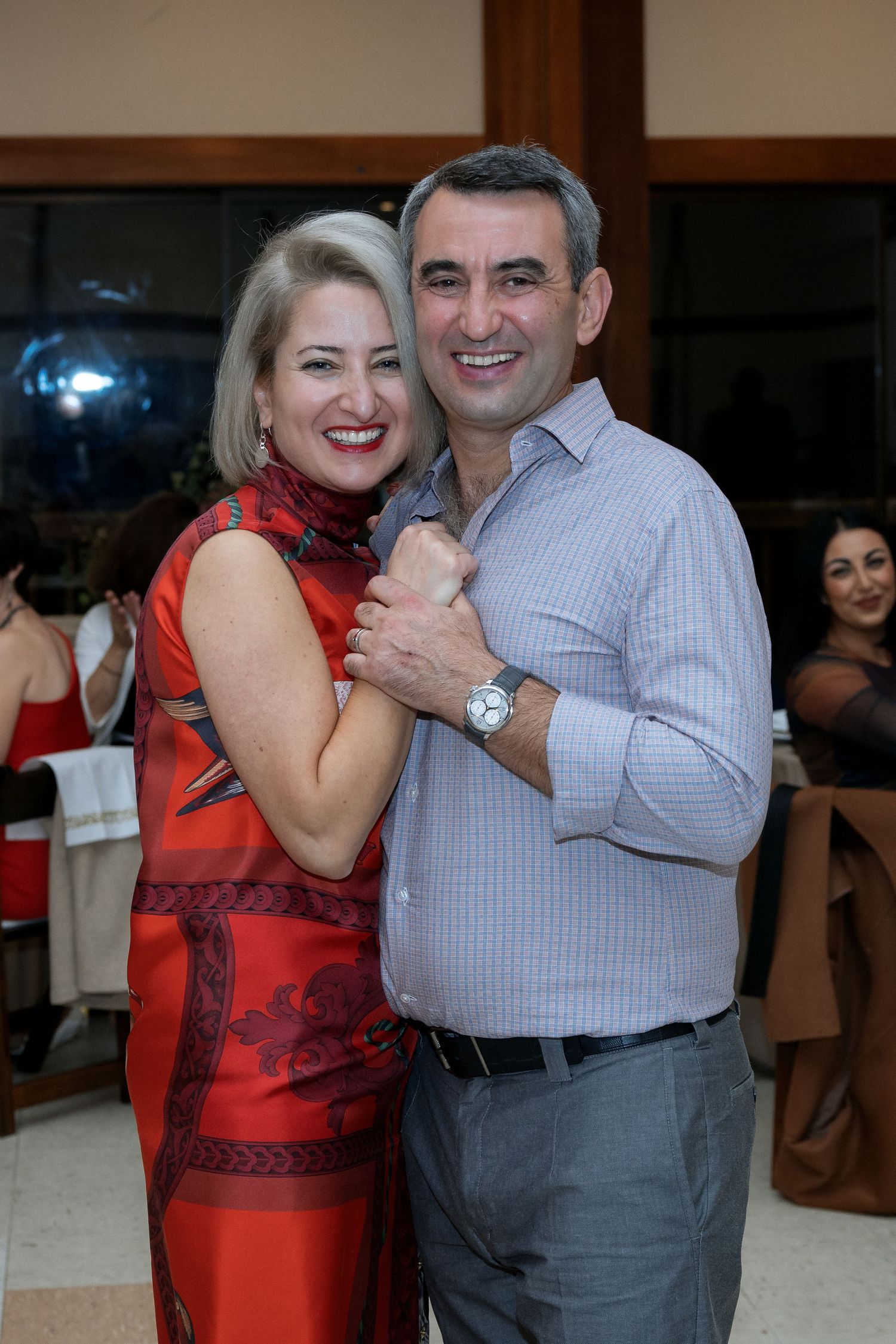 A couple dances together at an indoor celebration, both smiling brightly.
