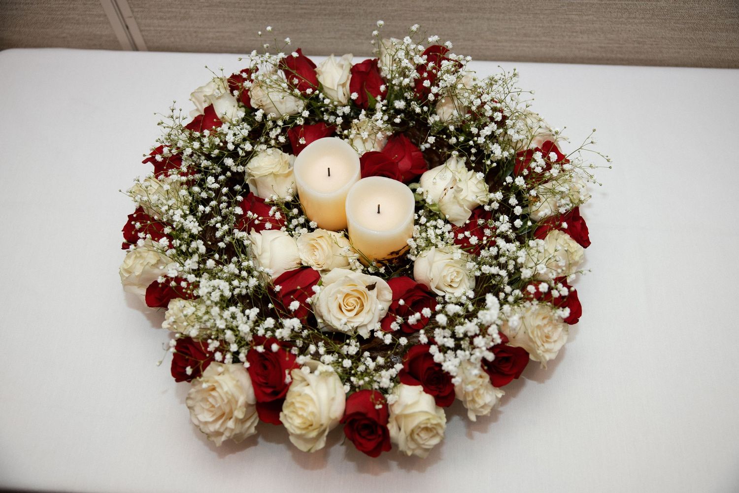 An elegant floral centerpiece with red and white roses arranged in a circle with white candles.