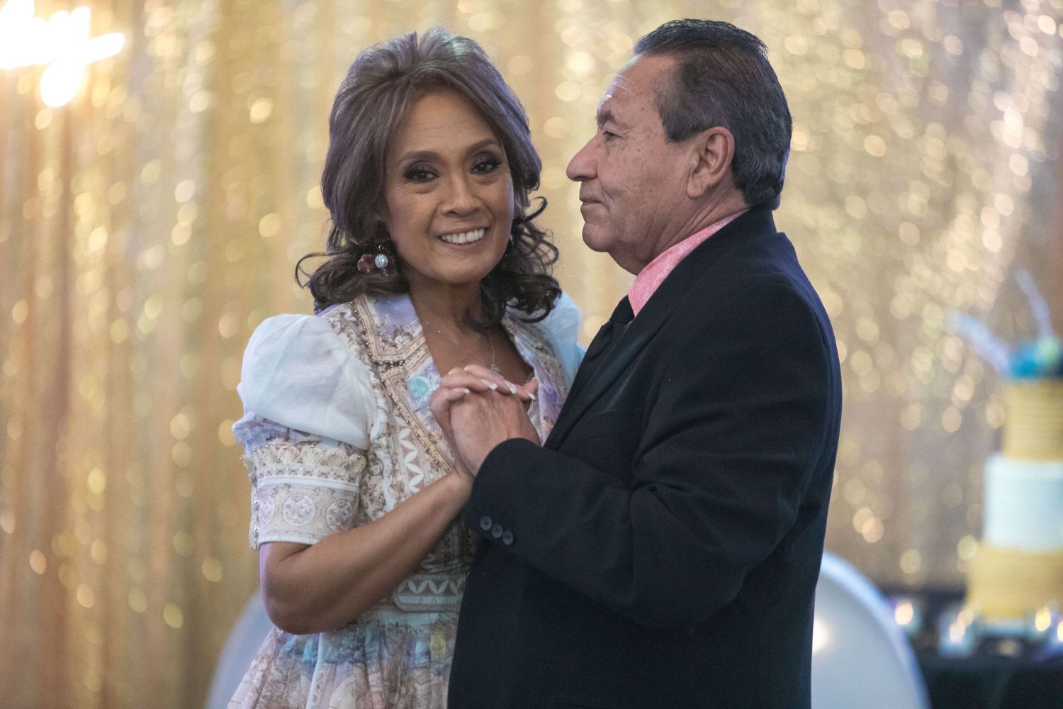 A couple shares a tender dance moment against a golden sparkly backdrop.