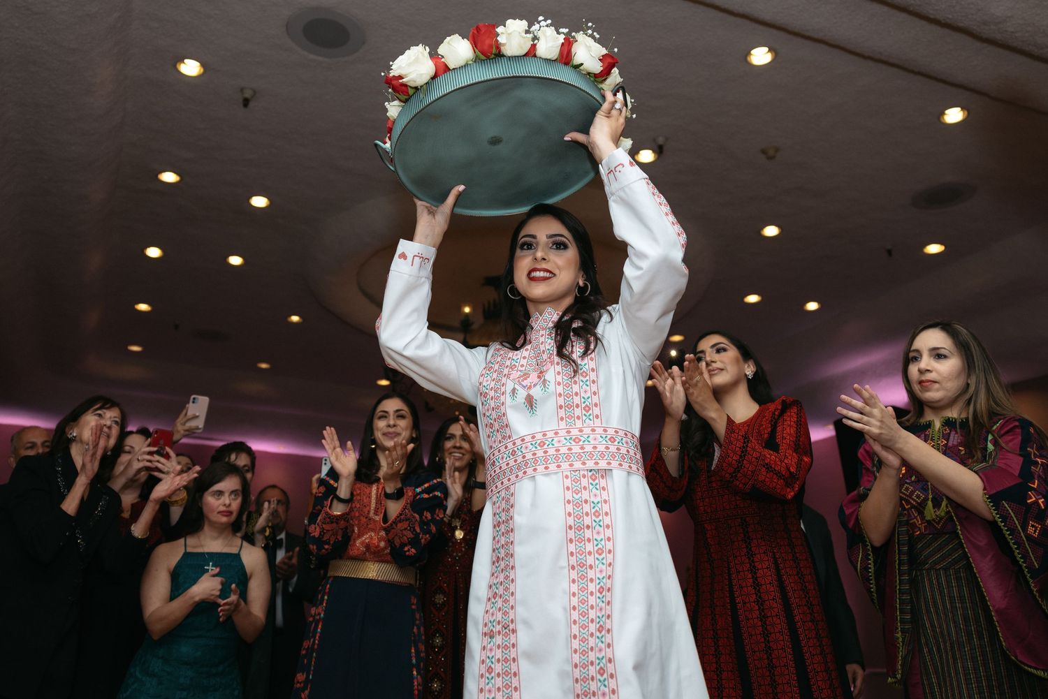 A person holds up a tray while others clap during a celebratory event.