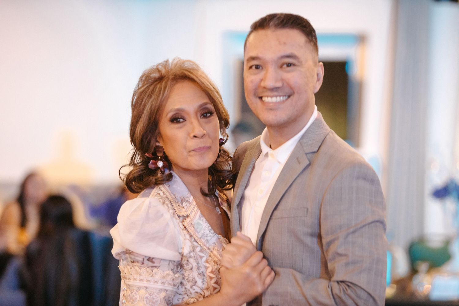 A couple poses together at an elegant indoor celebration with sparkling decor.