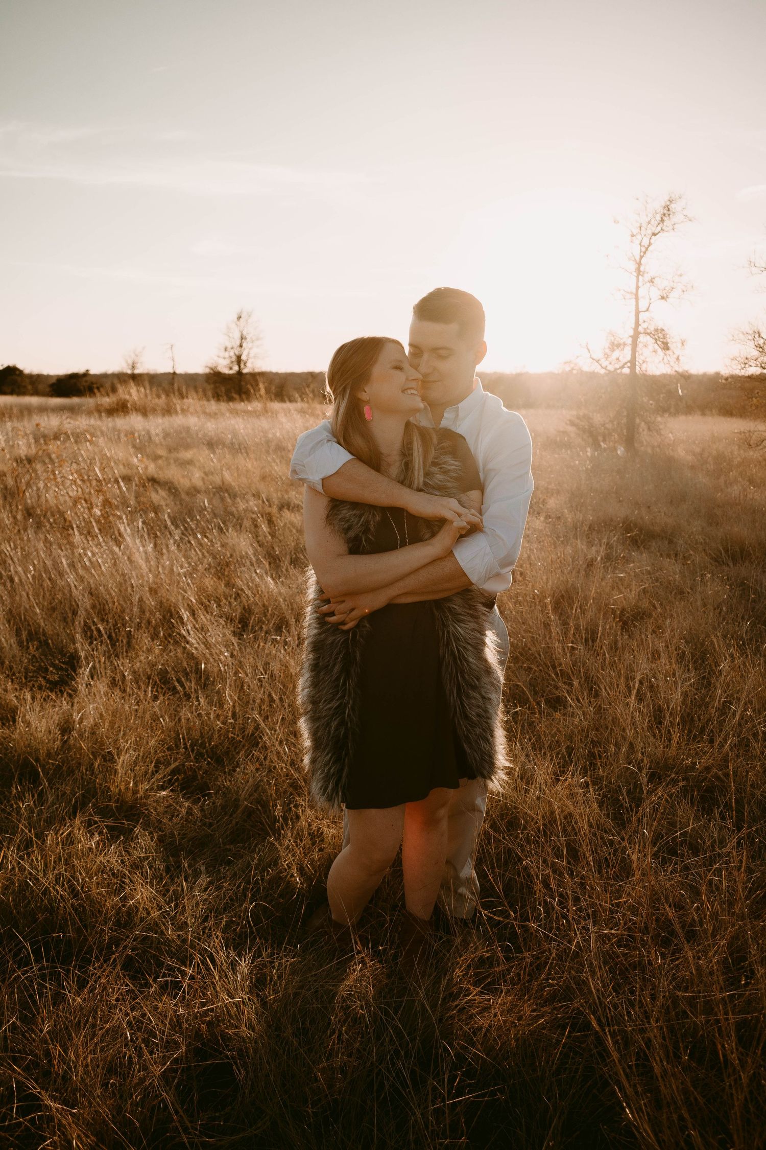 Couple shares intimate embrace in golden sunset light among tall prairie grass.
