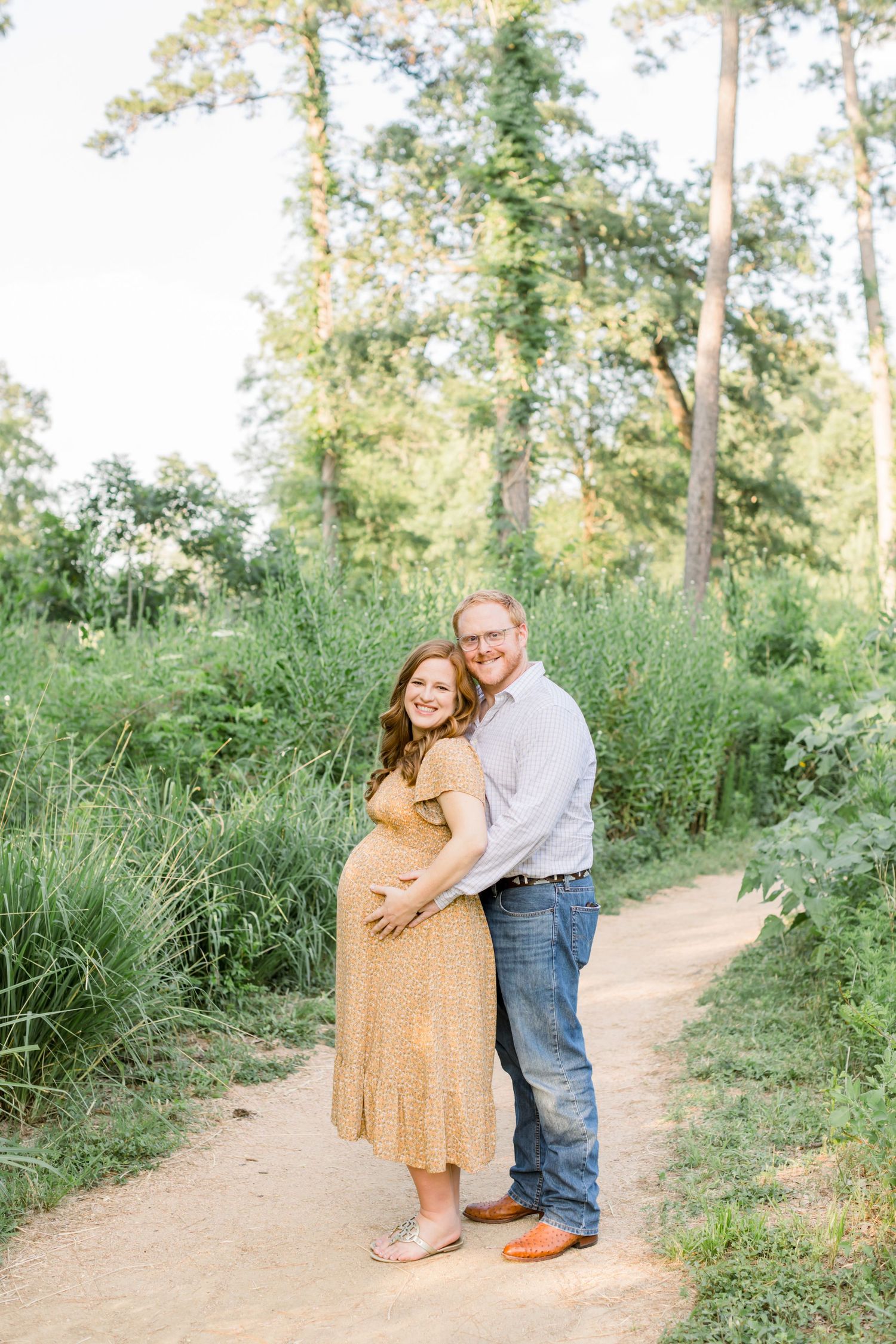 Couple embraces on nature trail during golden hour maternity photo session.