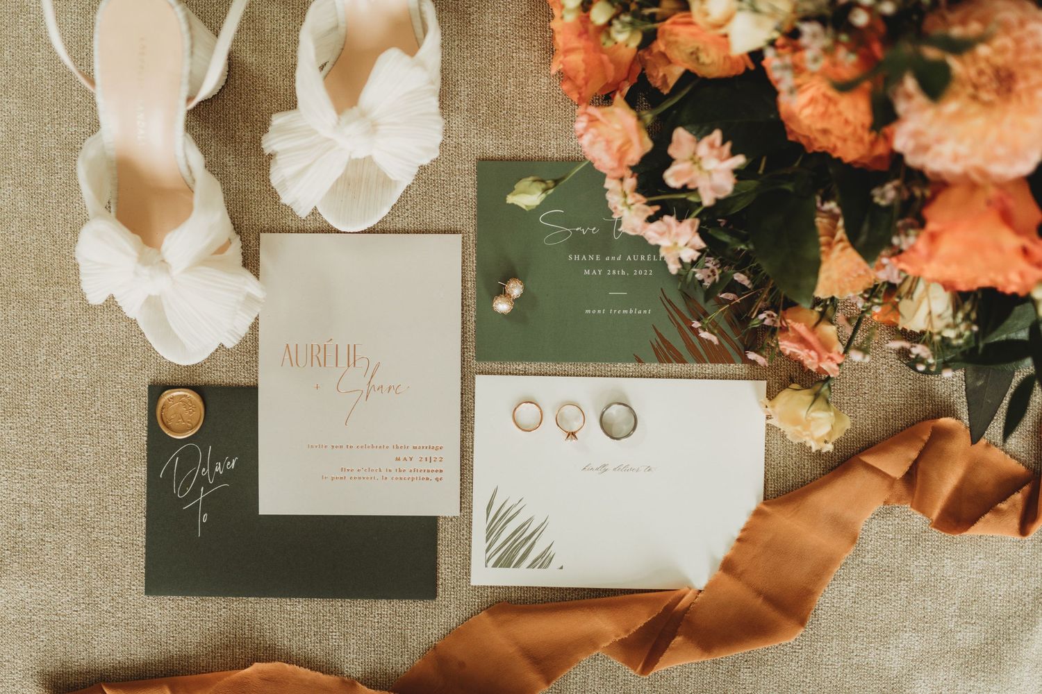 Wedding details including invitations, white shoes, and coral flowers on beige linen with copper ribbon accents.