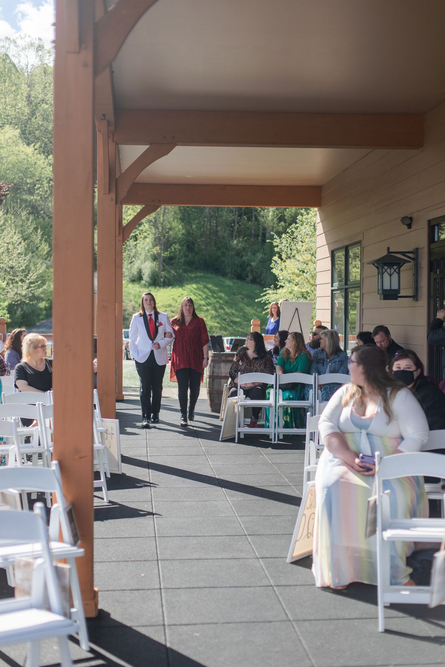 Wedding guests gathering under a covered outdoor venue with white chairs and decorations.