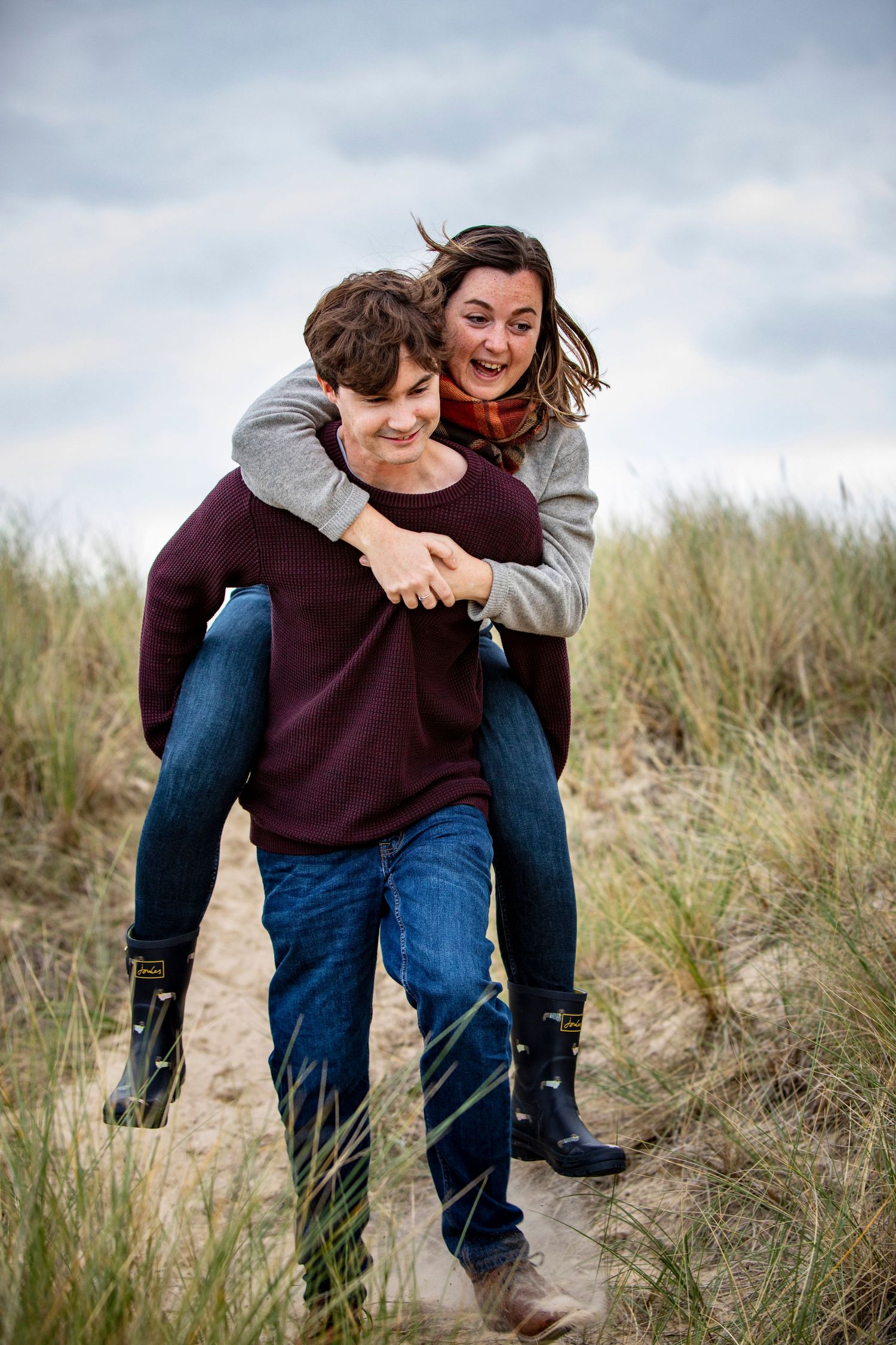 Couple playing and laughing together among coastal dune grass.