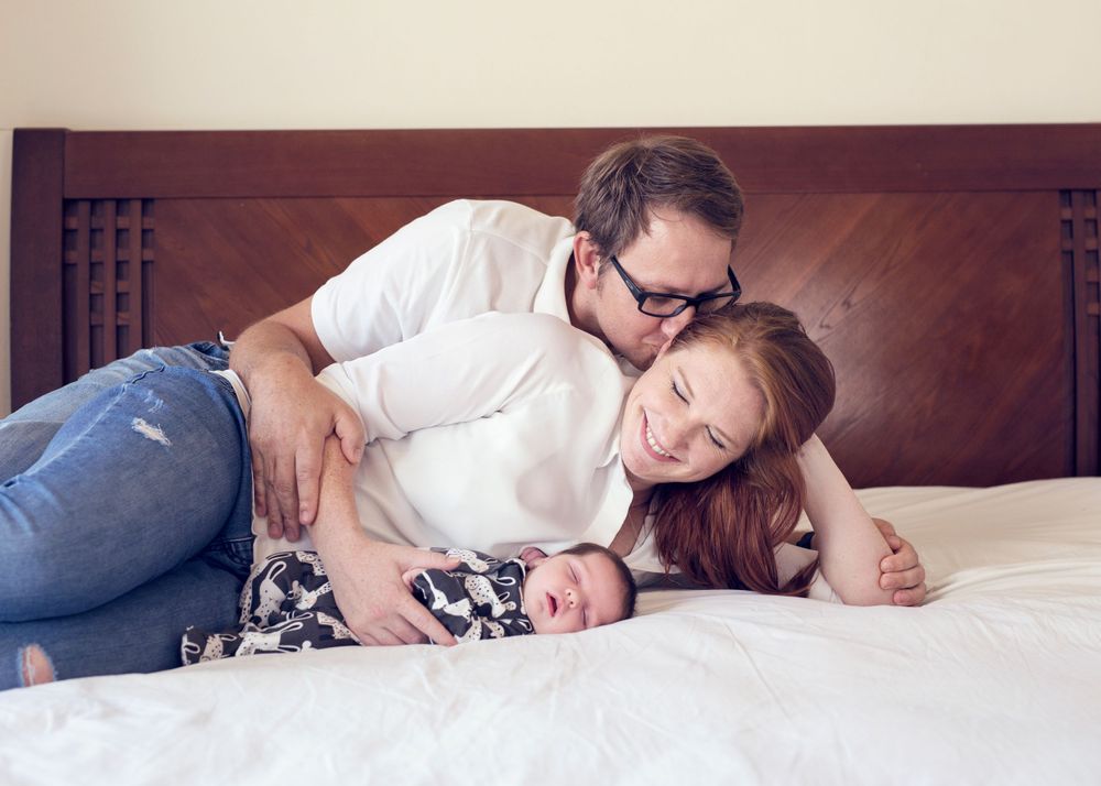 Dad giving Mom a loving kiss while Mom is looking at there newborn girl lying in her arms