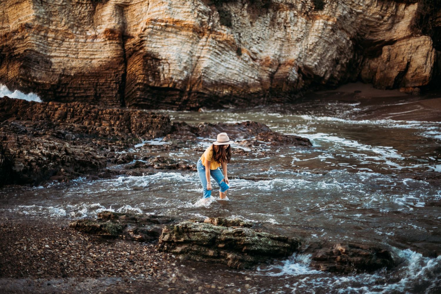 A person exploring rocky tide pools along a dramatic coastal shoreline.