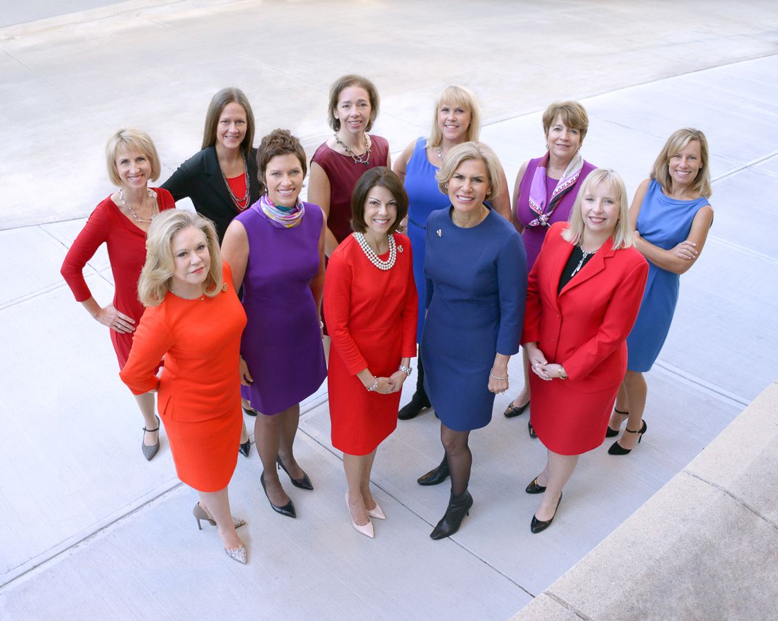 Group of professionals wearing colorful dresses posed together in a V formation.