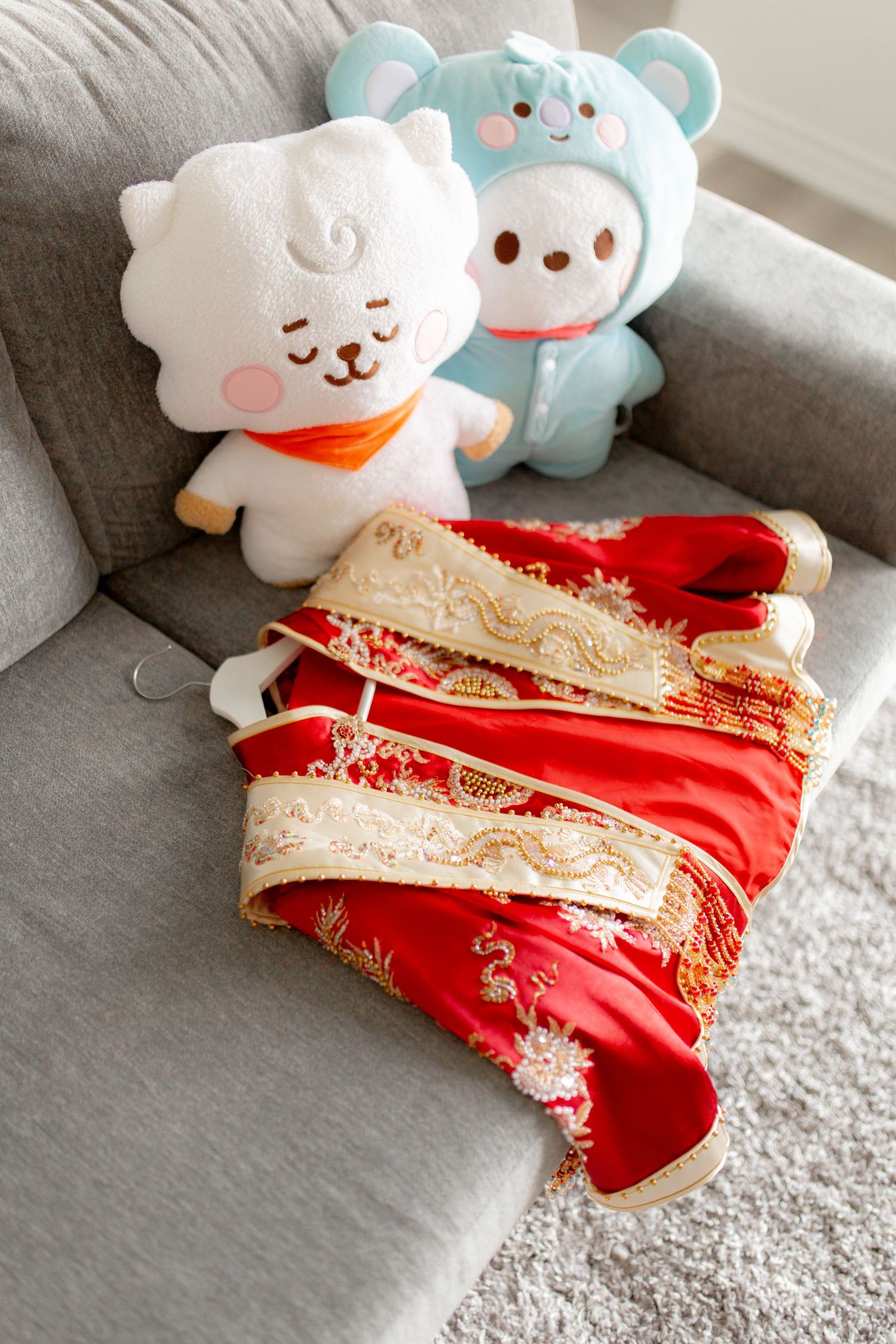 Cute plush toys and traditional red Chinese wedding dress displayed on gray couch.