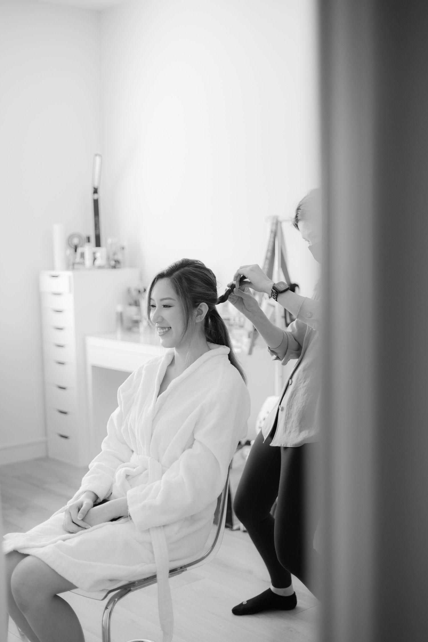 Black and white photo of bridal preparation with hair styling in progress.