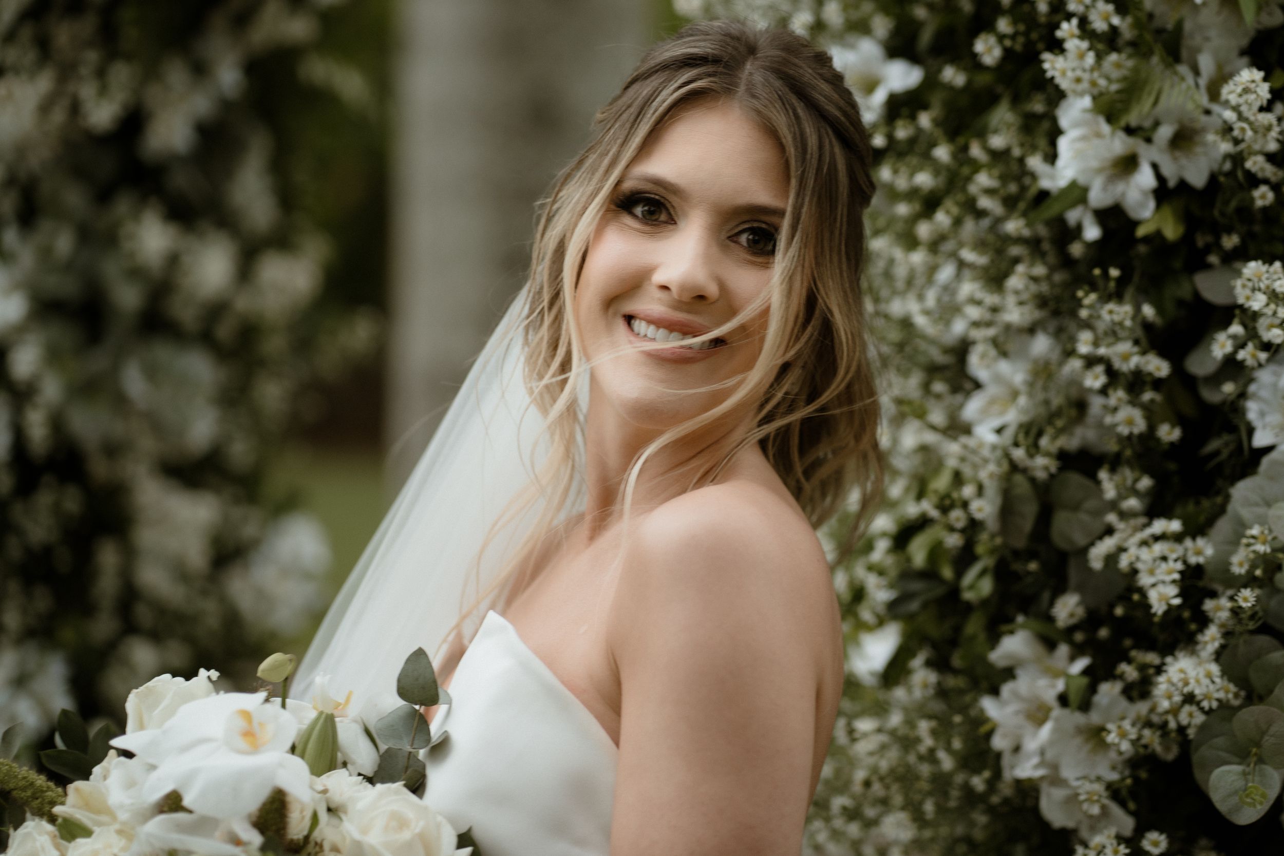 Portrait of bride in strapless gown holding white bouquet amidst flowering trees.