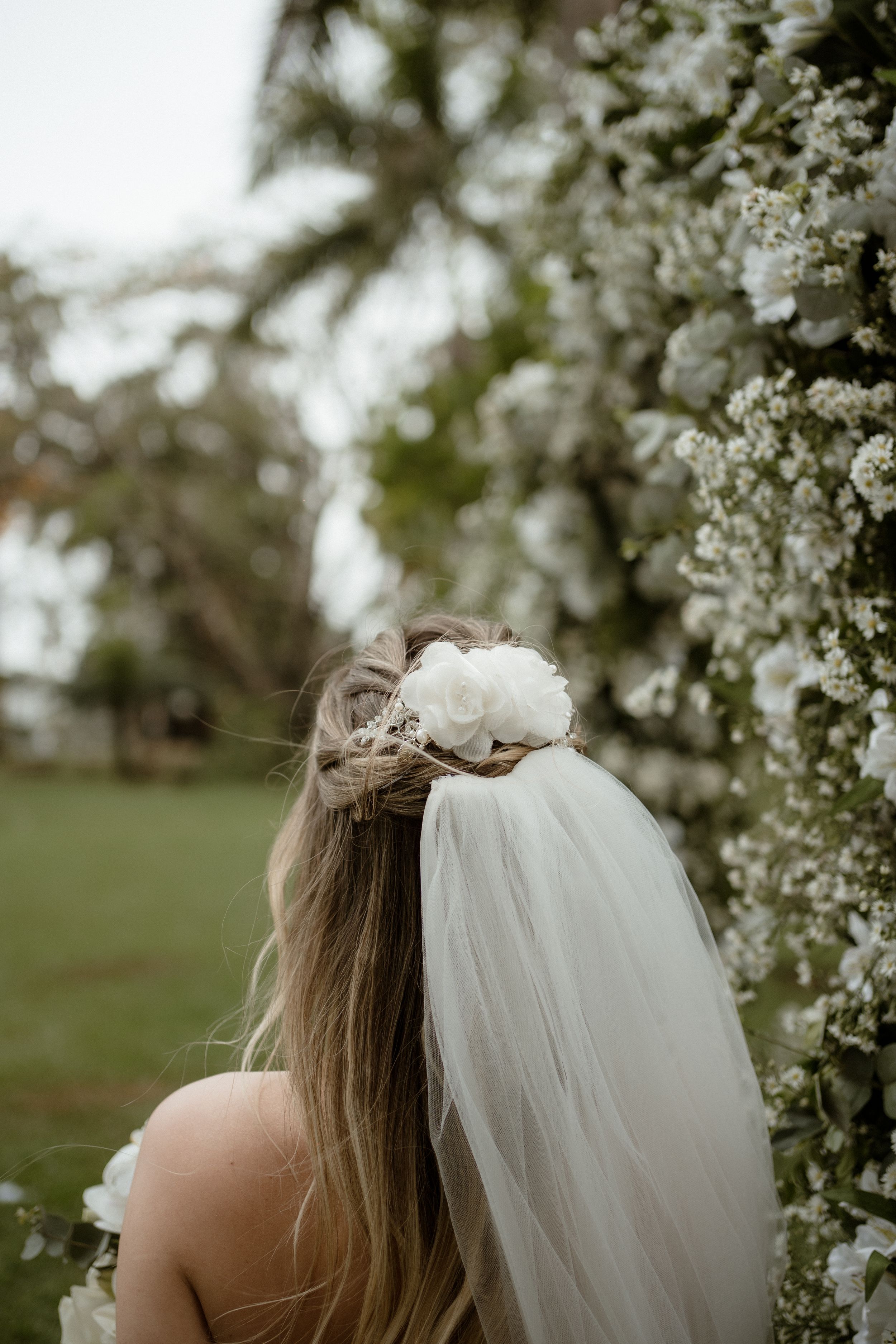 Close-up of bride's delicate veil and floral hair accessory against blooming white flowers.