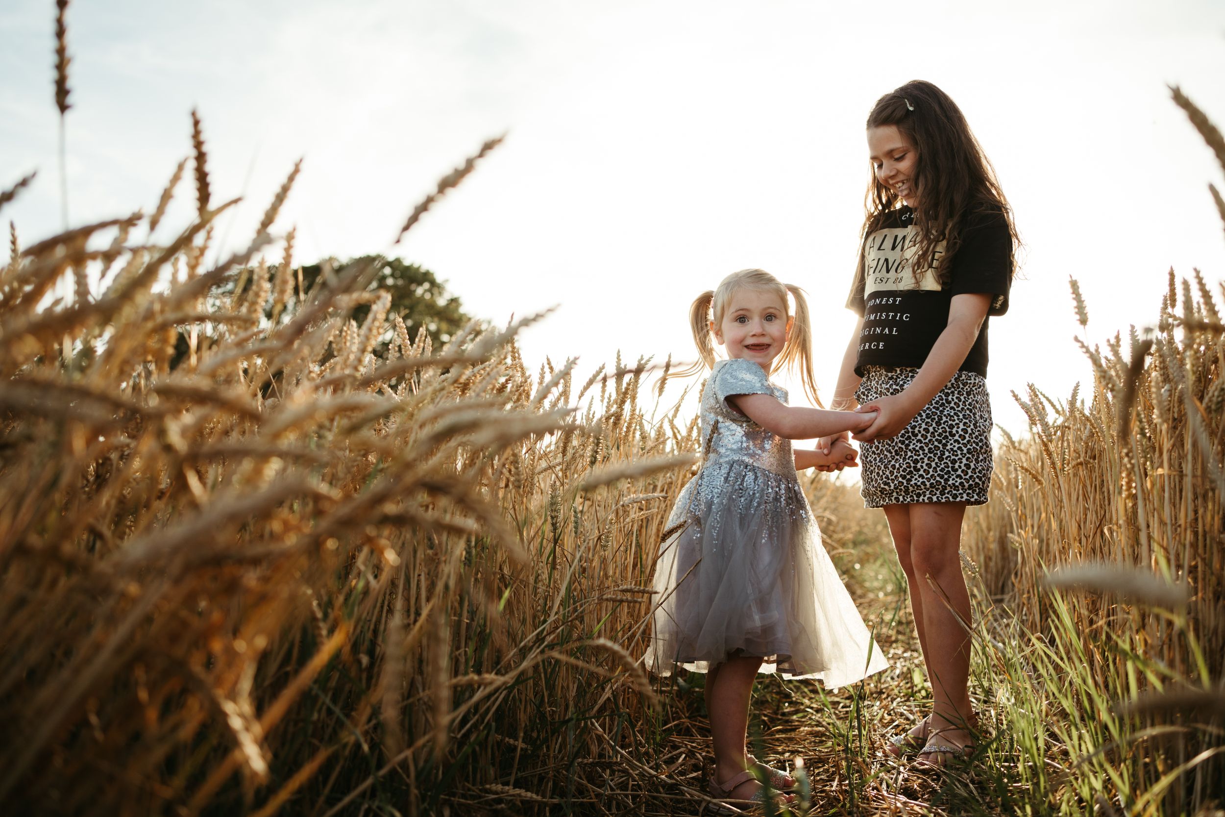 Two people walking through a golden wheat field at sunset.